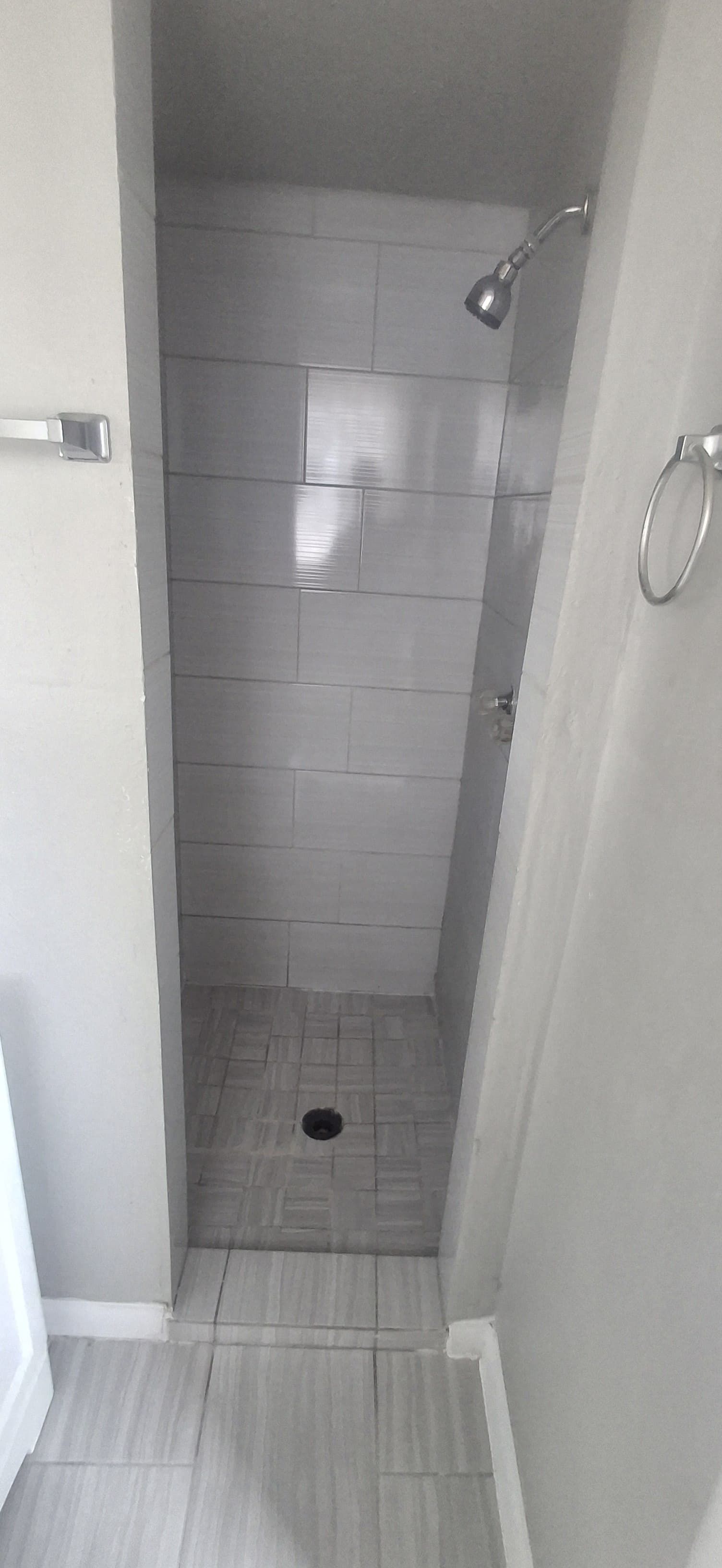 Narrow shower with gray tile, showerhead, and drain.