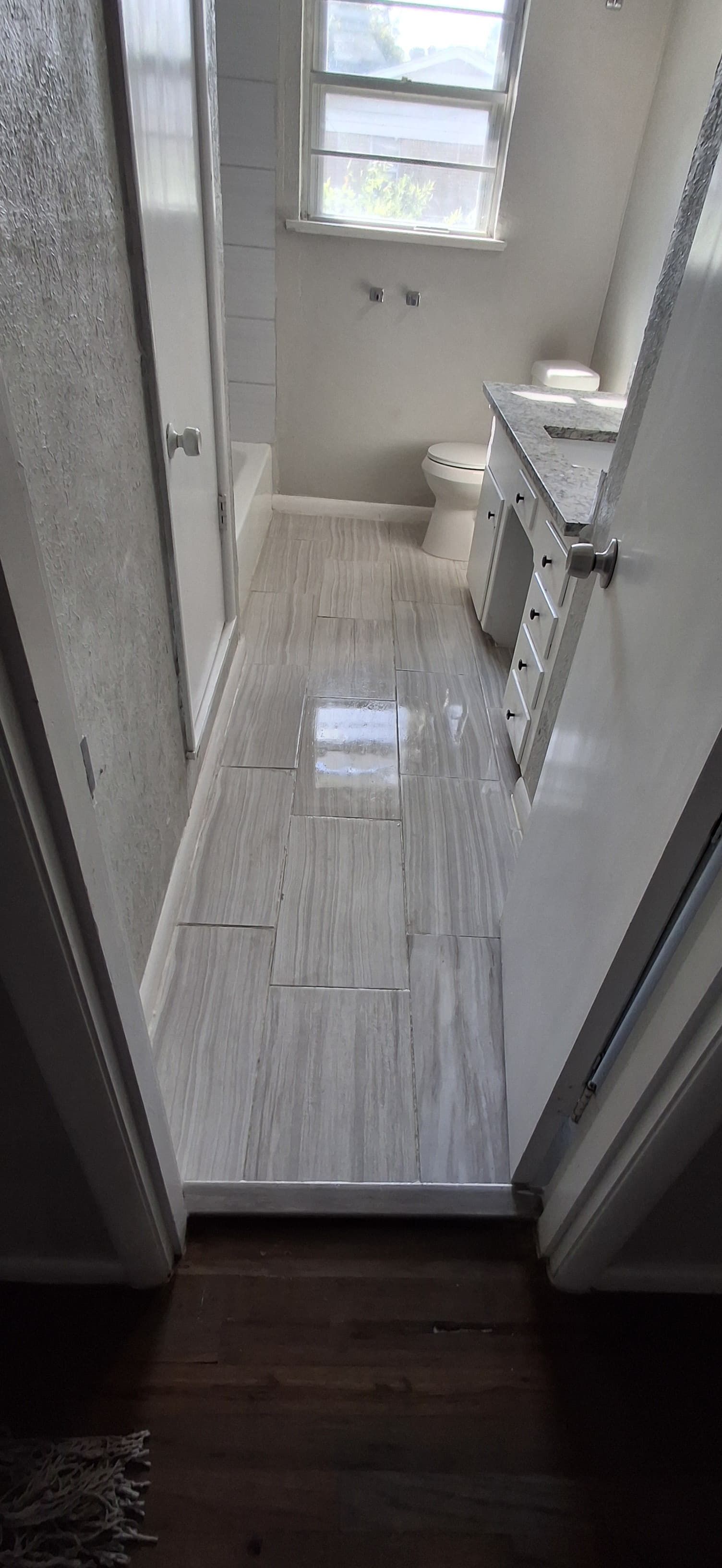 Bathroom interior, looking down the length of the room with a window at the end and a shower stall to the left.
