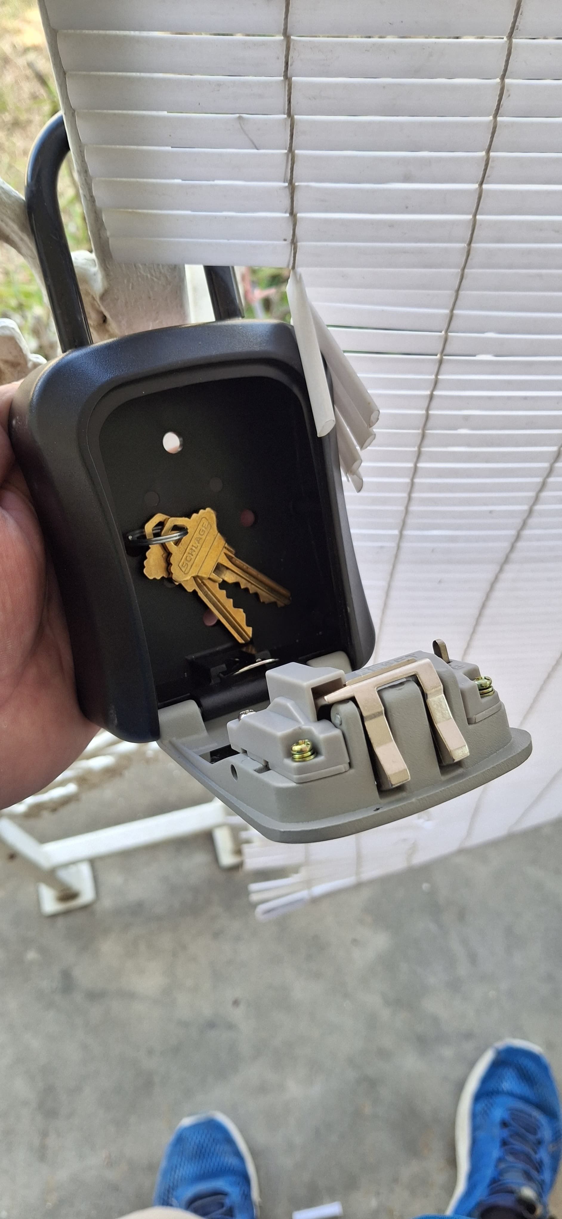 A person holding an open black key lockbox with keys inside, near white blinds.