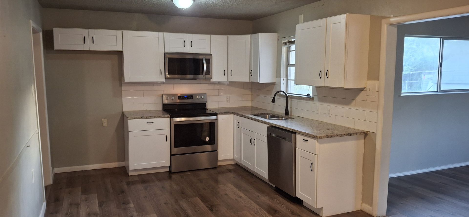 A newly renovated kitchen with white cabinets, stainless steel appliances, and wood floors.