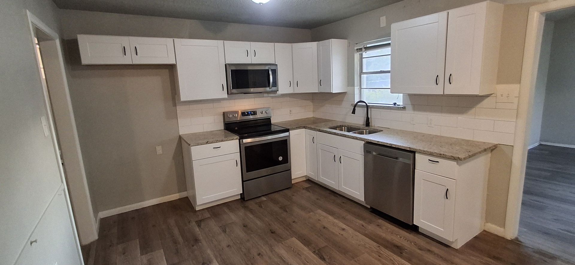 White kitchen with stainless steel appliances and wood-look flooring.