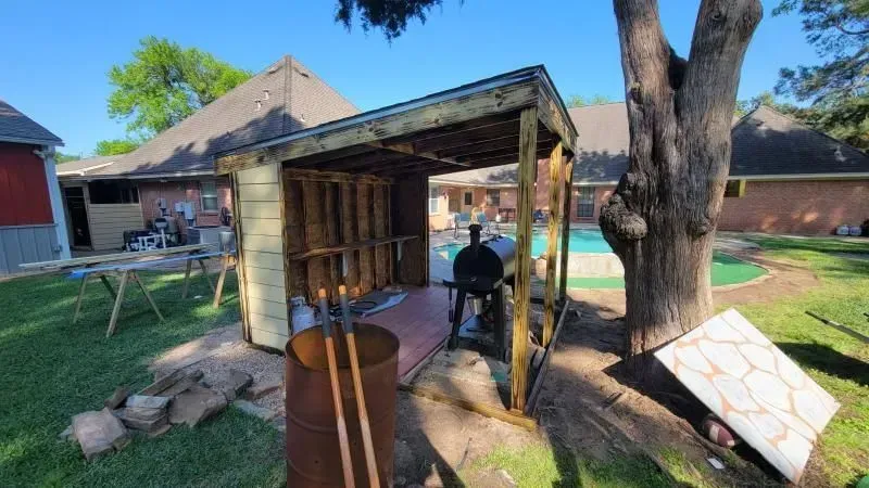 Wooden outdoor grilling station with grill, in a backyard setting near a pool, under a tree.
