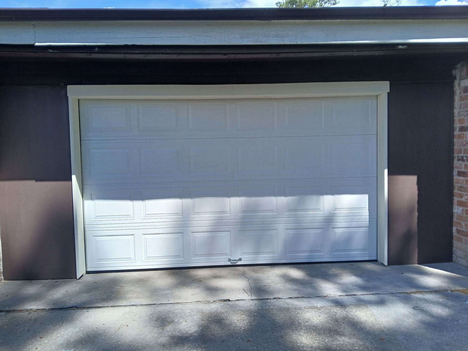 White garage door in a brown building, concrete driveway.