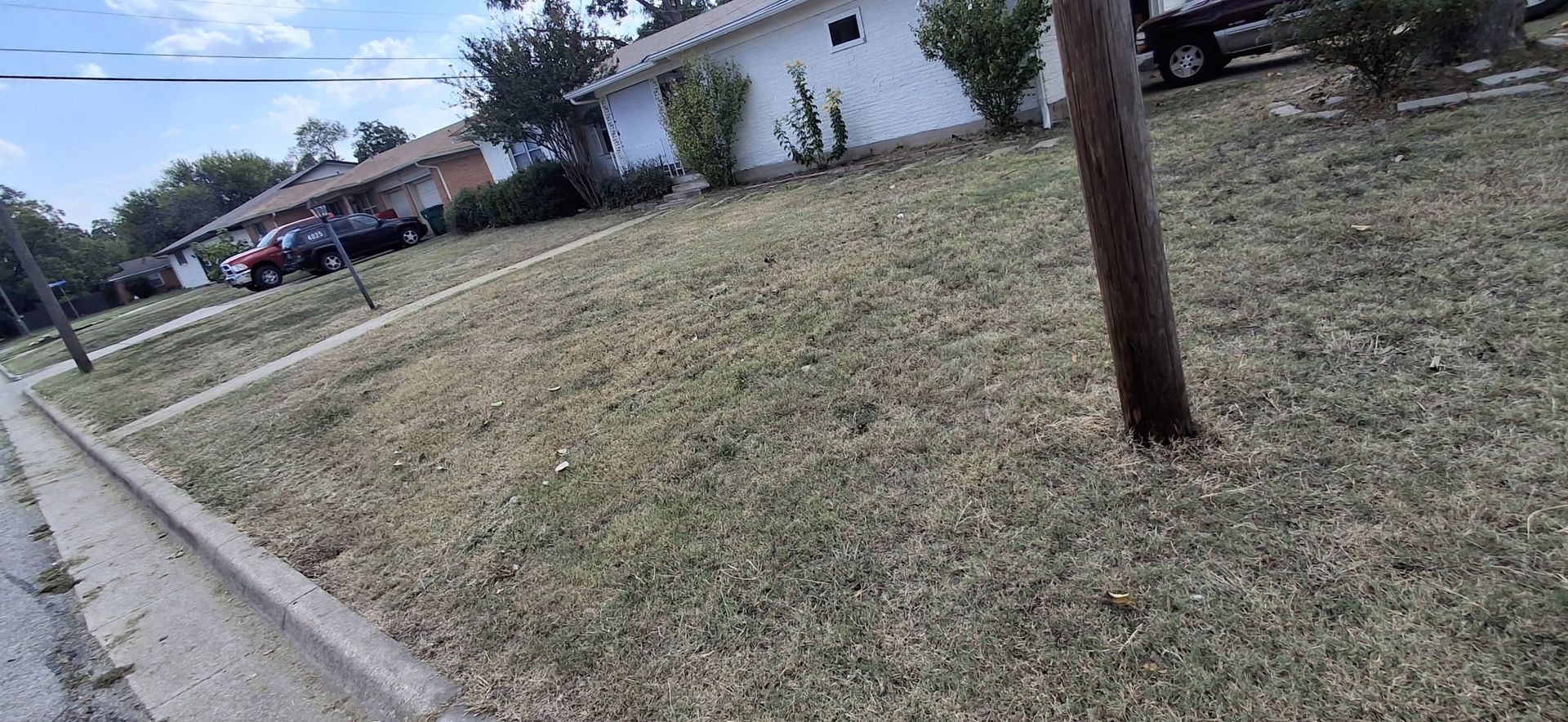 A neighborhood street scene, with houses and dry grass in front. A power pole is on the right side.