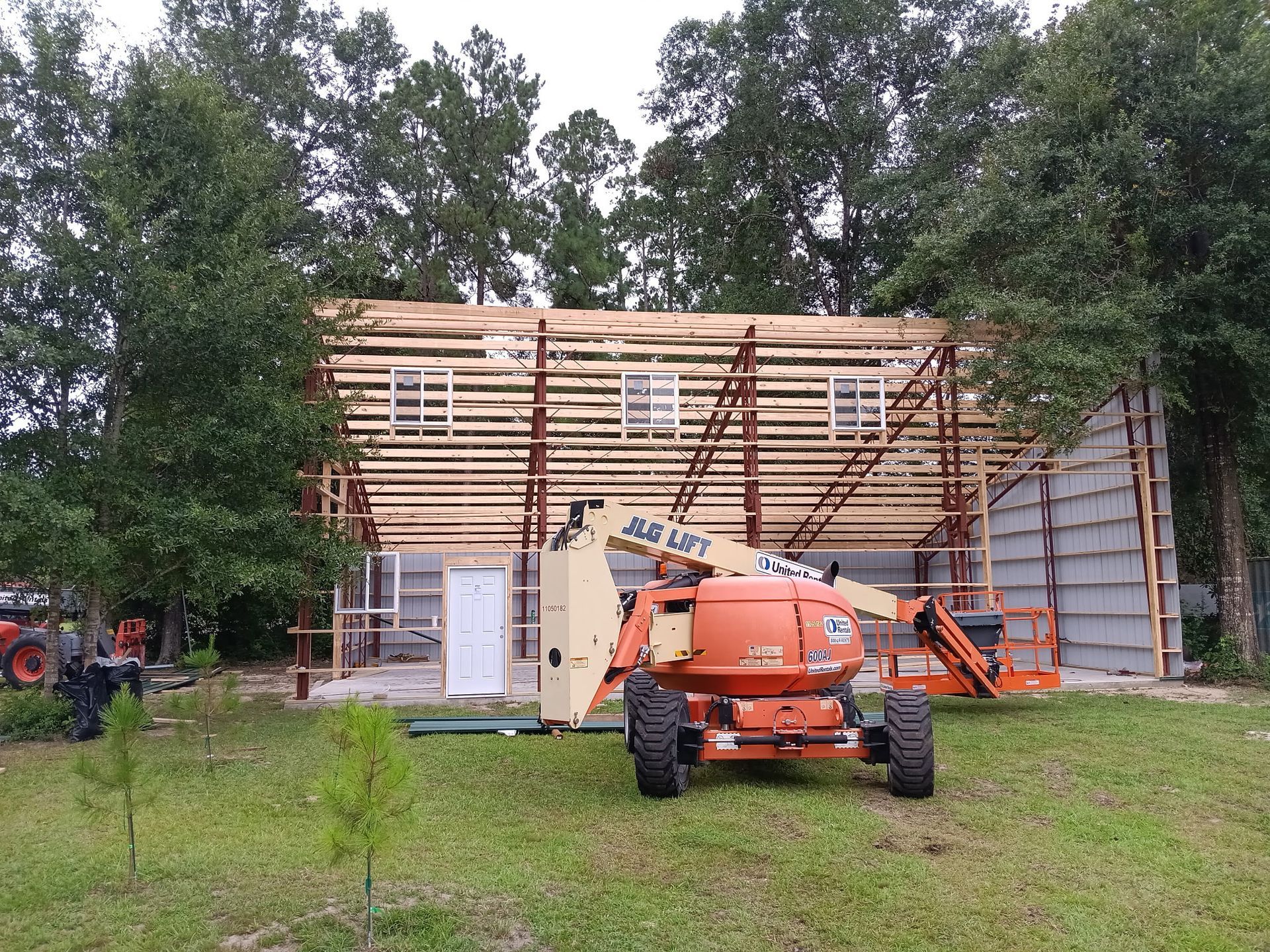 Construction site with an orange lift, a partially built metal building, and trees.