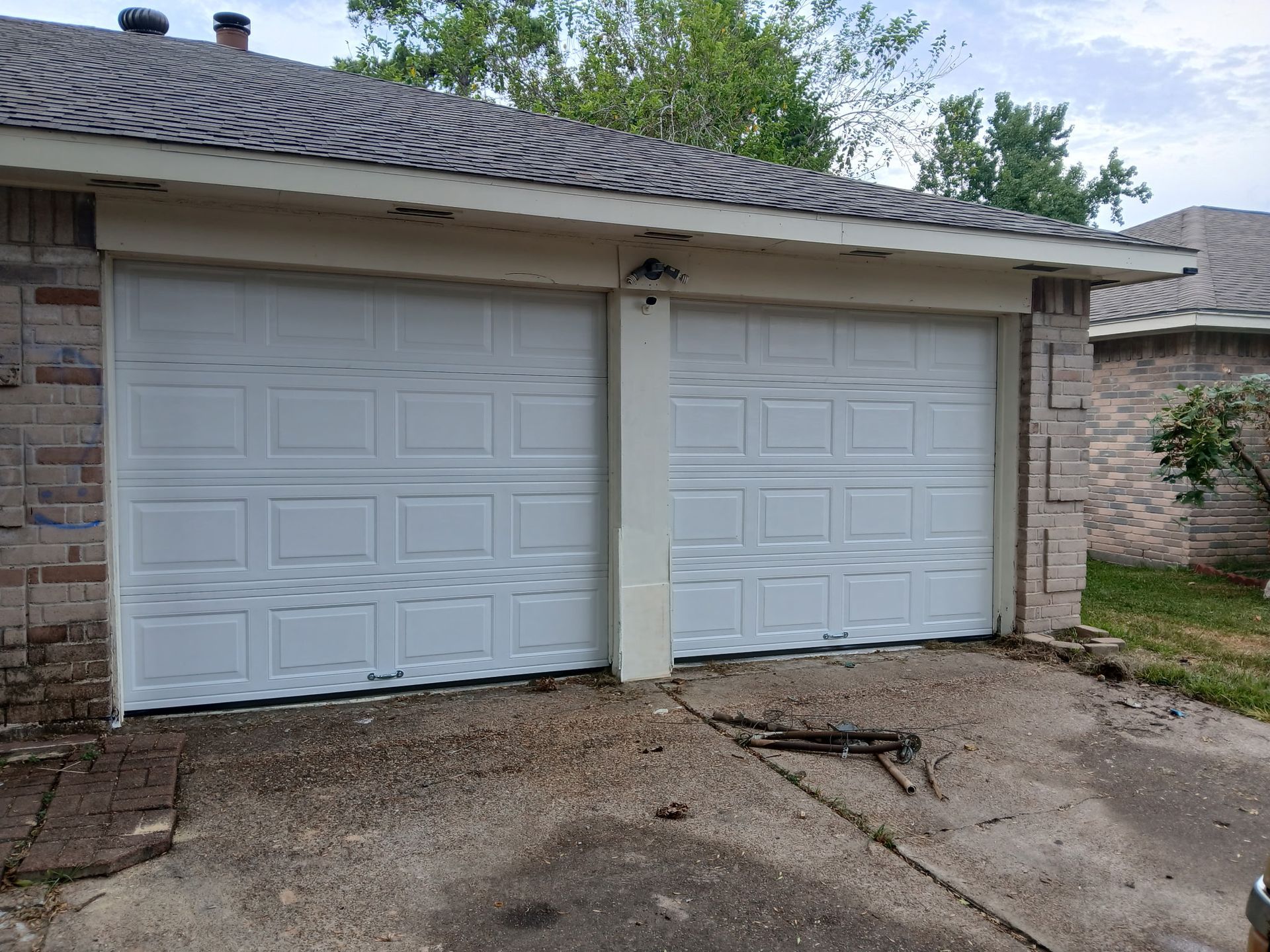 Two white garage doors on a house with a concrete driveway. Brick and tan trim surround.