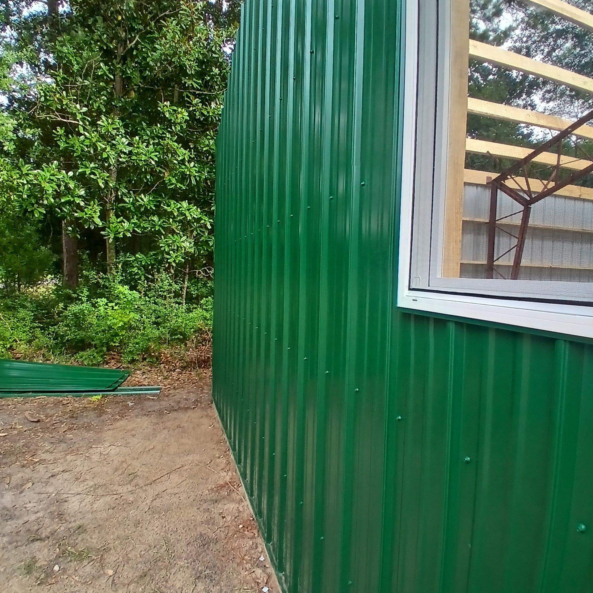 Green corrugated metal siding on a building with a partially constructed window.