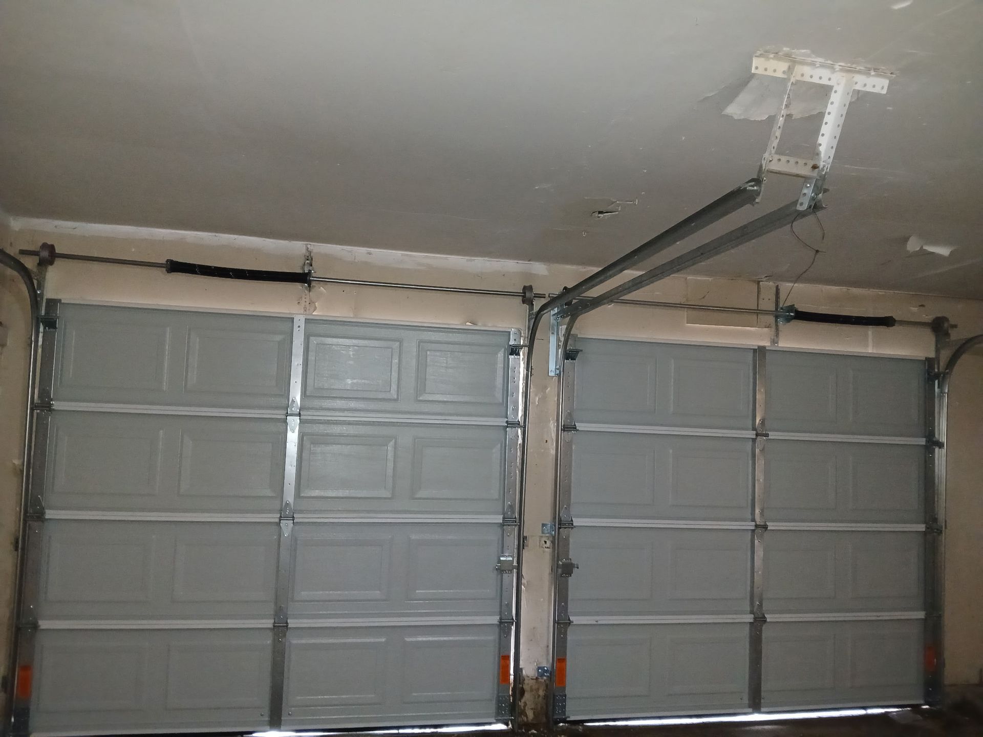 Two gray garage doors side-by-side inside a garage. A ceiling-mounted garage door opener is visible above.