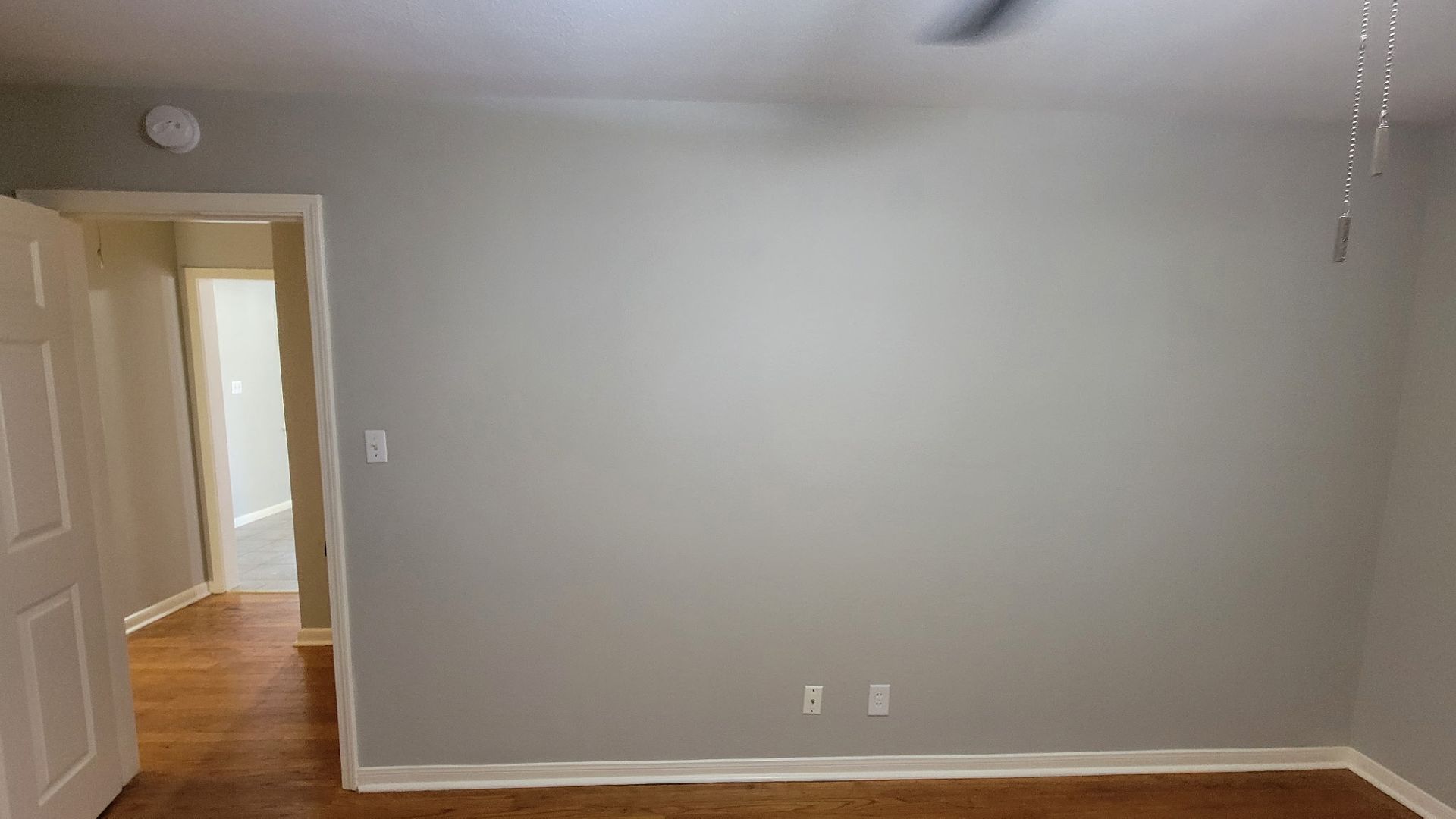 Empty bedroom with gray walls, doorway, and wood-look flooring.