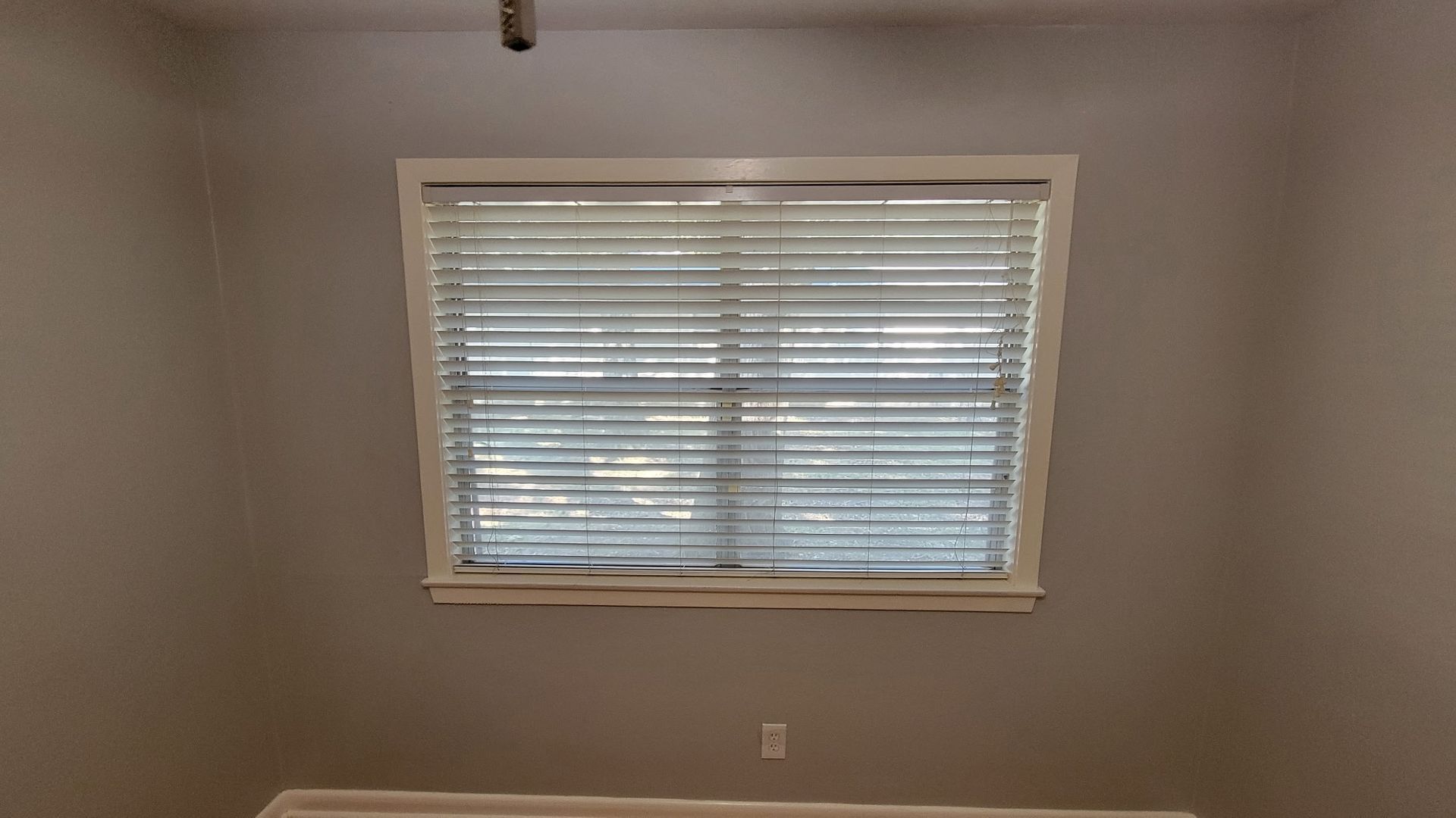 Window with closed blinds in a room with gray walls and a white window frame.