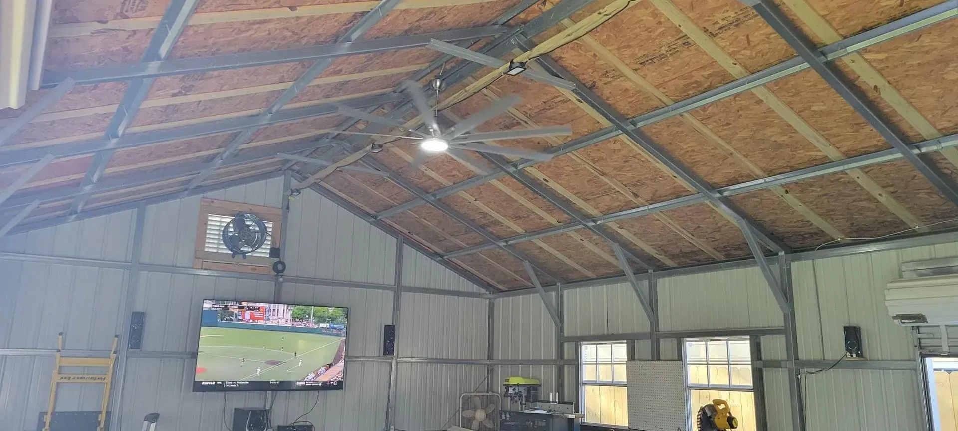 Interior of a large metal building with a TV, ceiling fan, and windows.