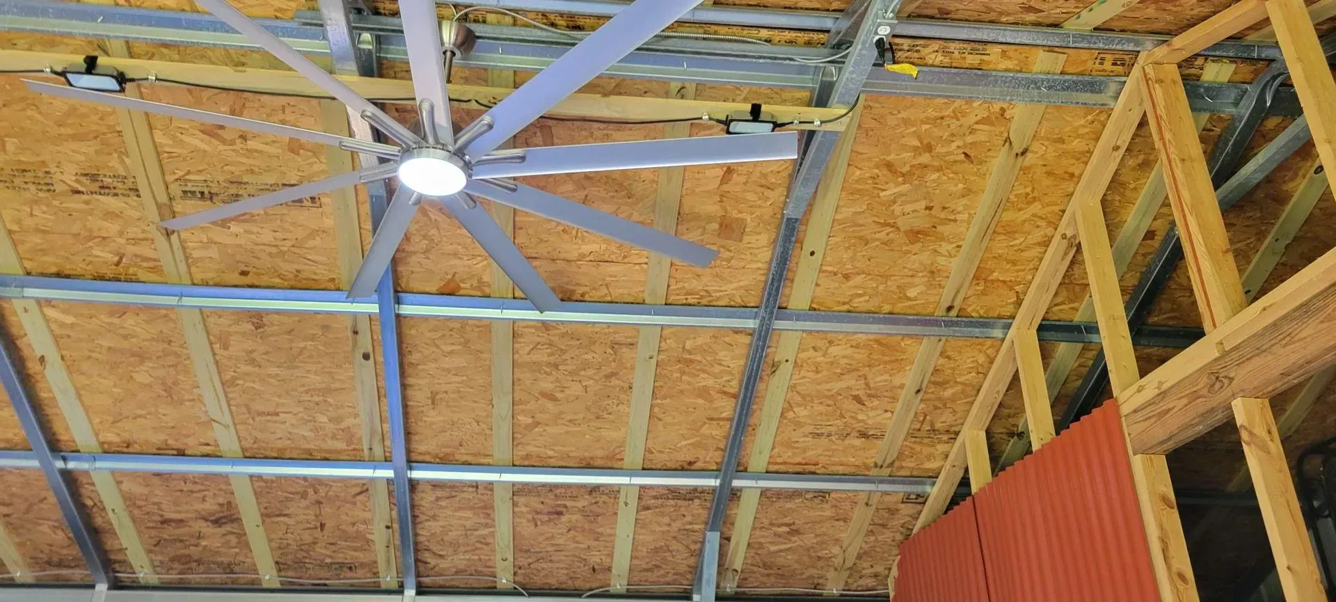Ceiling of a building under construction, featuring a large fan, wood panels, and metal framing.