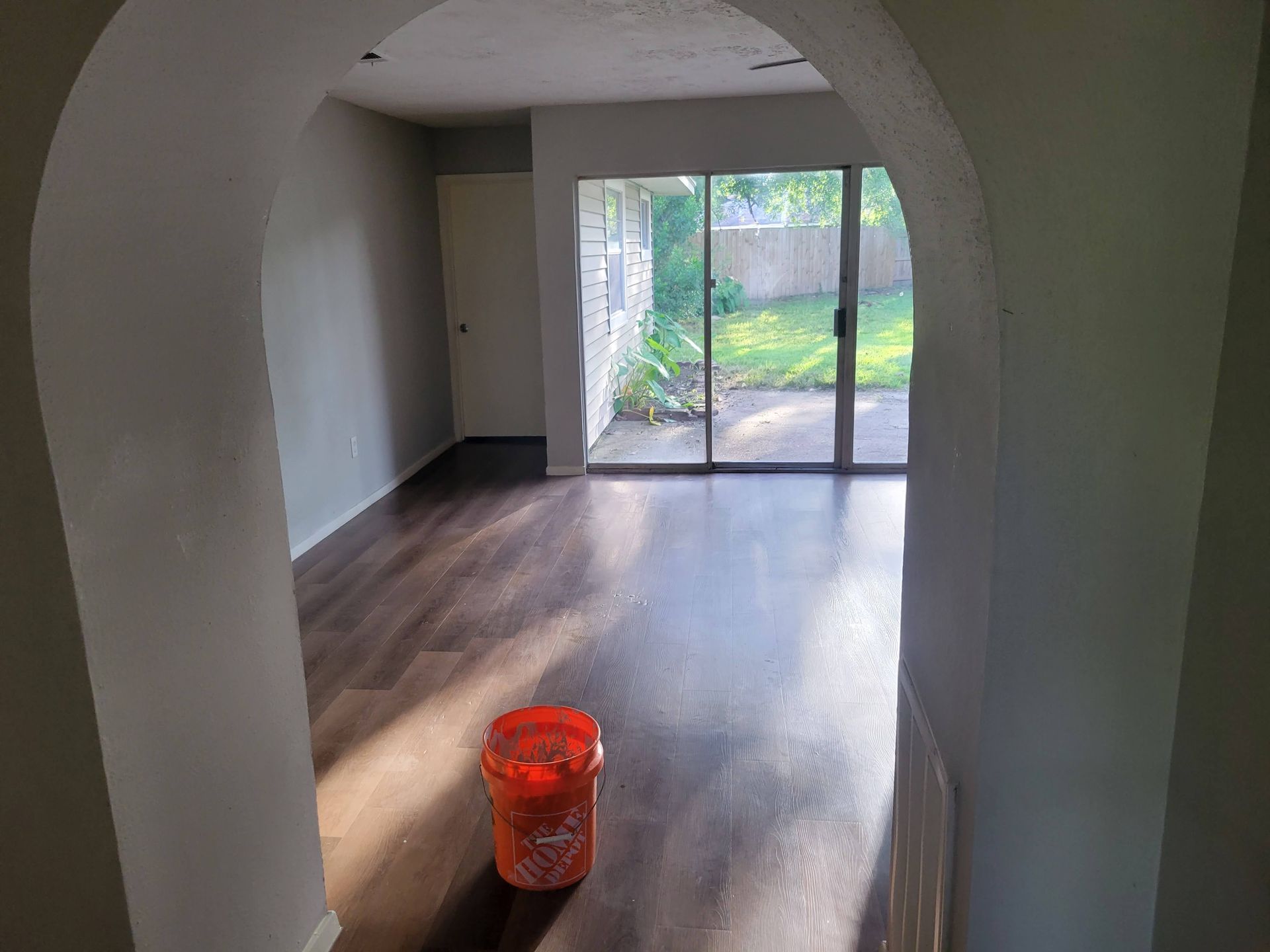Interior view through an archway, hardwood floors, a sliding glass door to a yard, and a bucket.