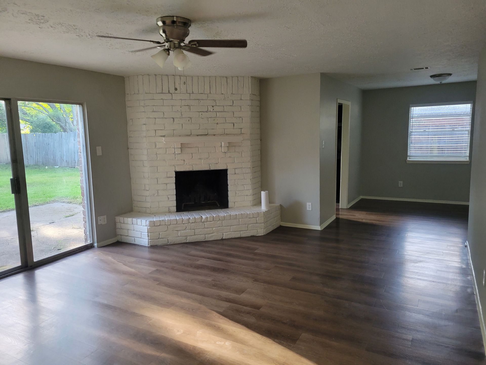 Living room with painted brick fireplace, sliding glass door, and dark wood-look flooring.