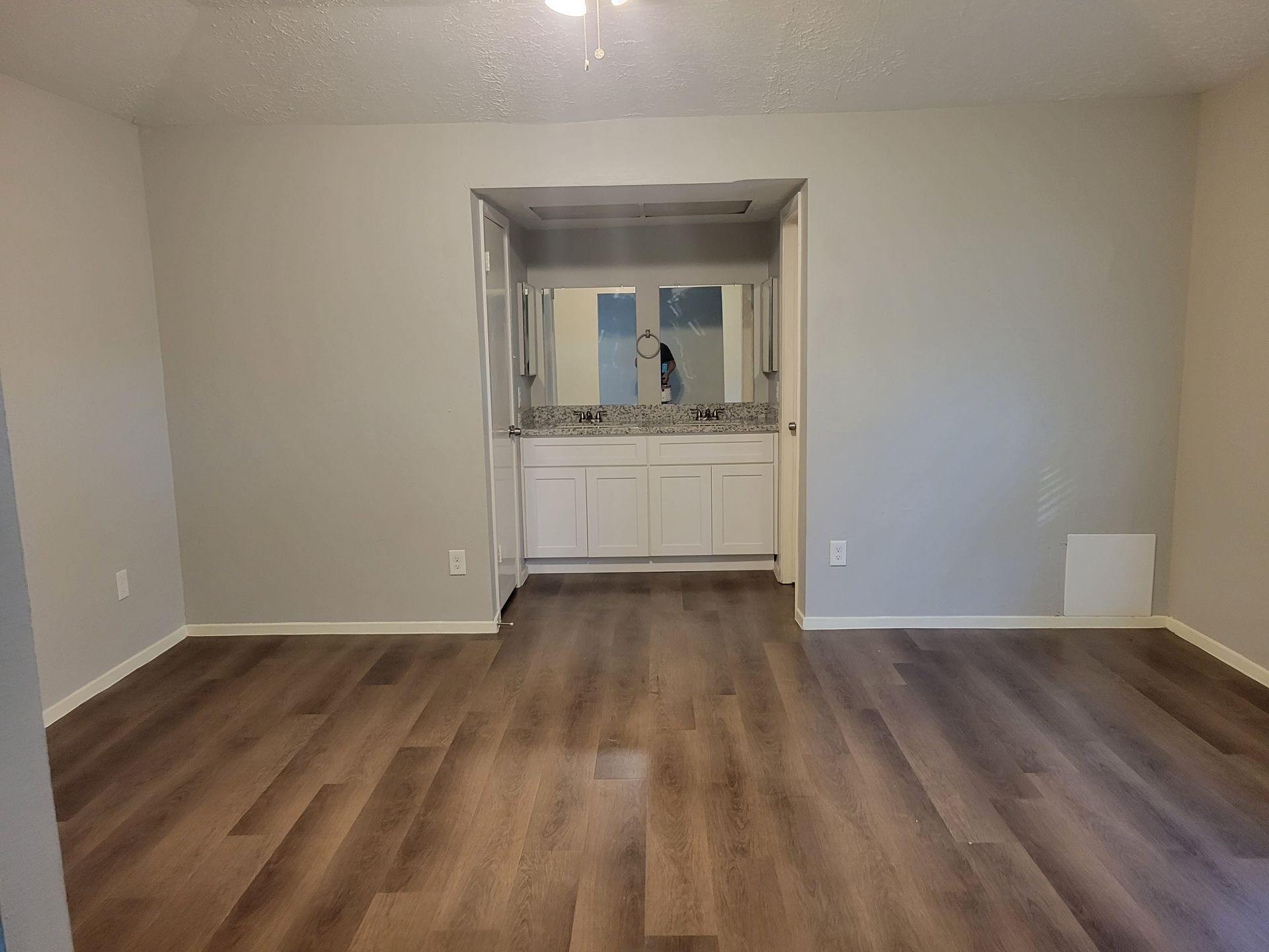 Bedroom with wood-look flooring and a bathroom visible through a doorway with a white vanity and silver mirror.