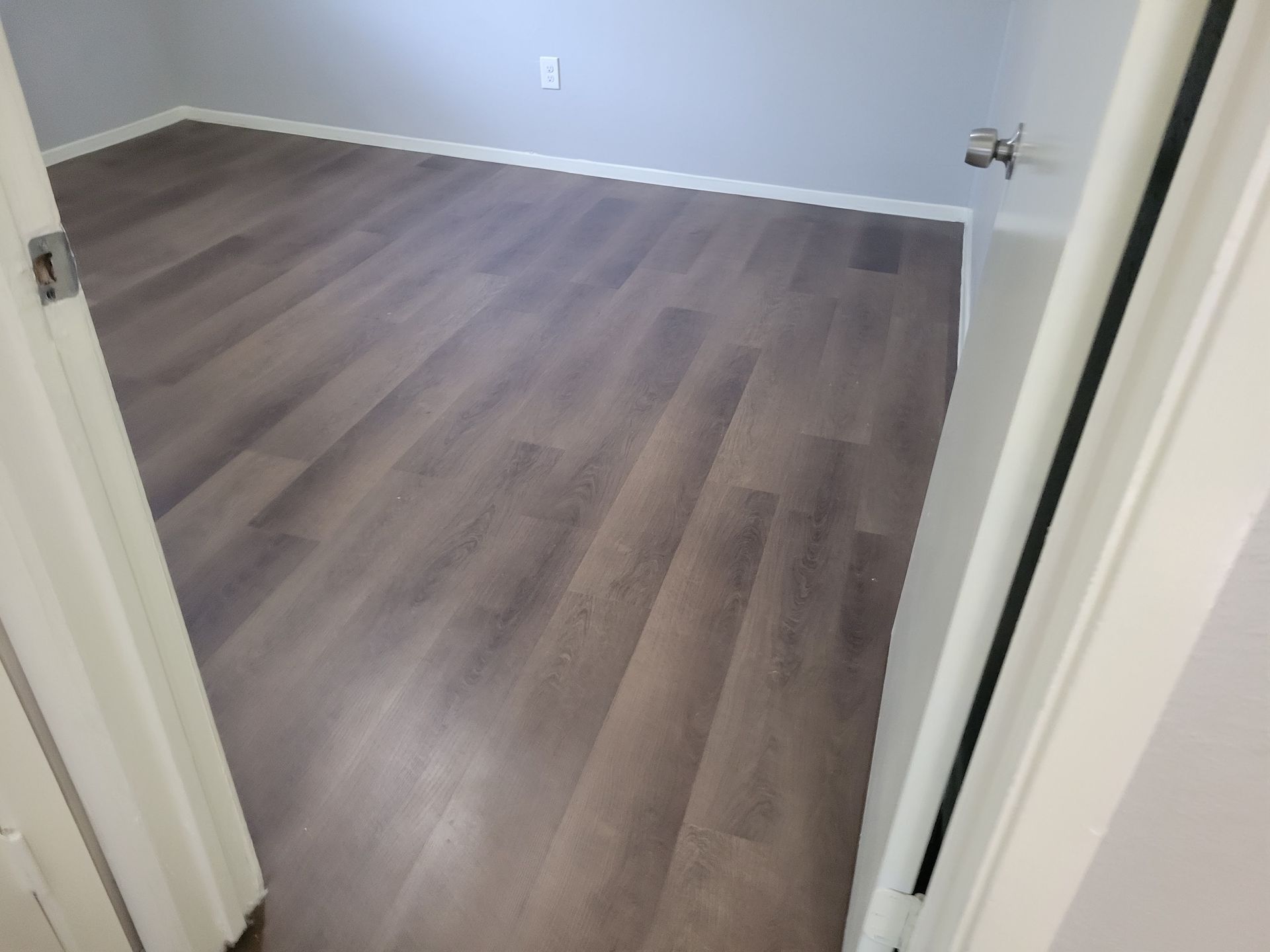 Empty room with gray wood-look flooring. White trim and door frame.