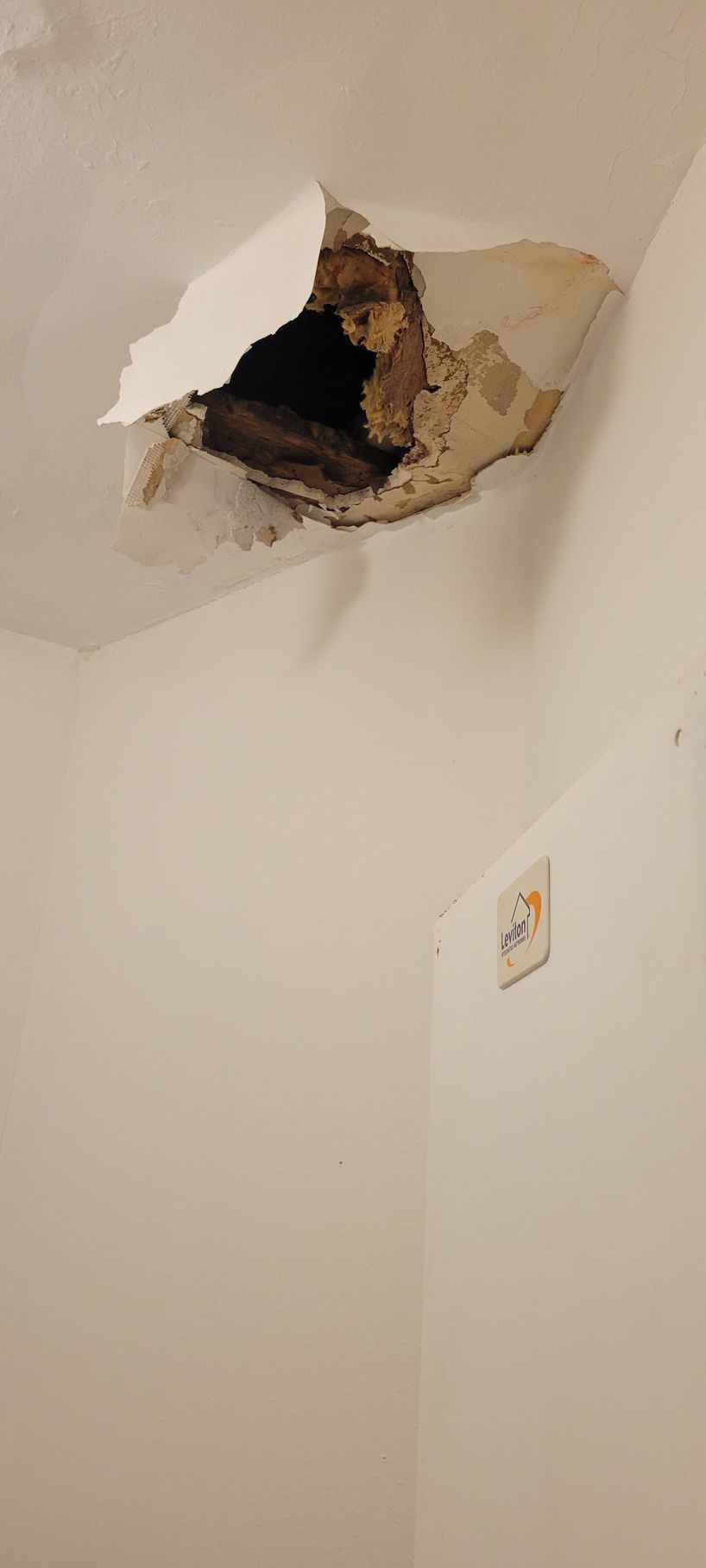 Hole in ceiling with damaged plaster exposing the structure above. A wall outlet is visible below.