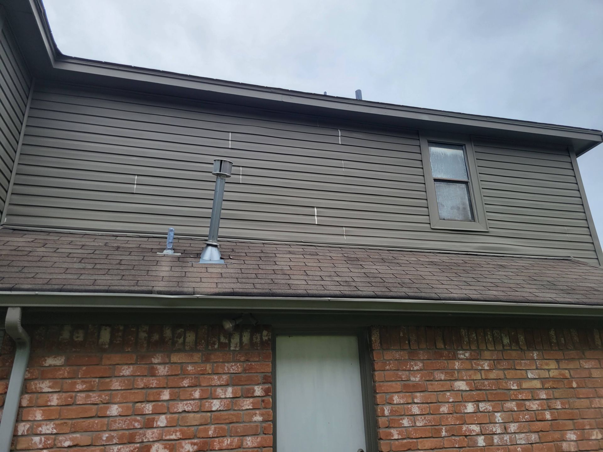 Exterior view of a two-story brick and siding house with chimney pipes on the roof. Brown siding and roof.