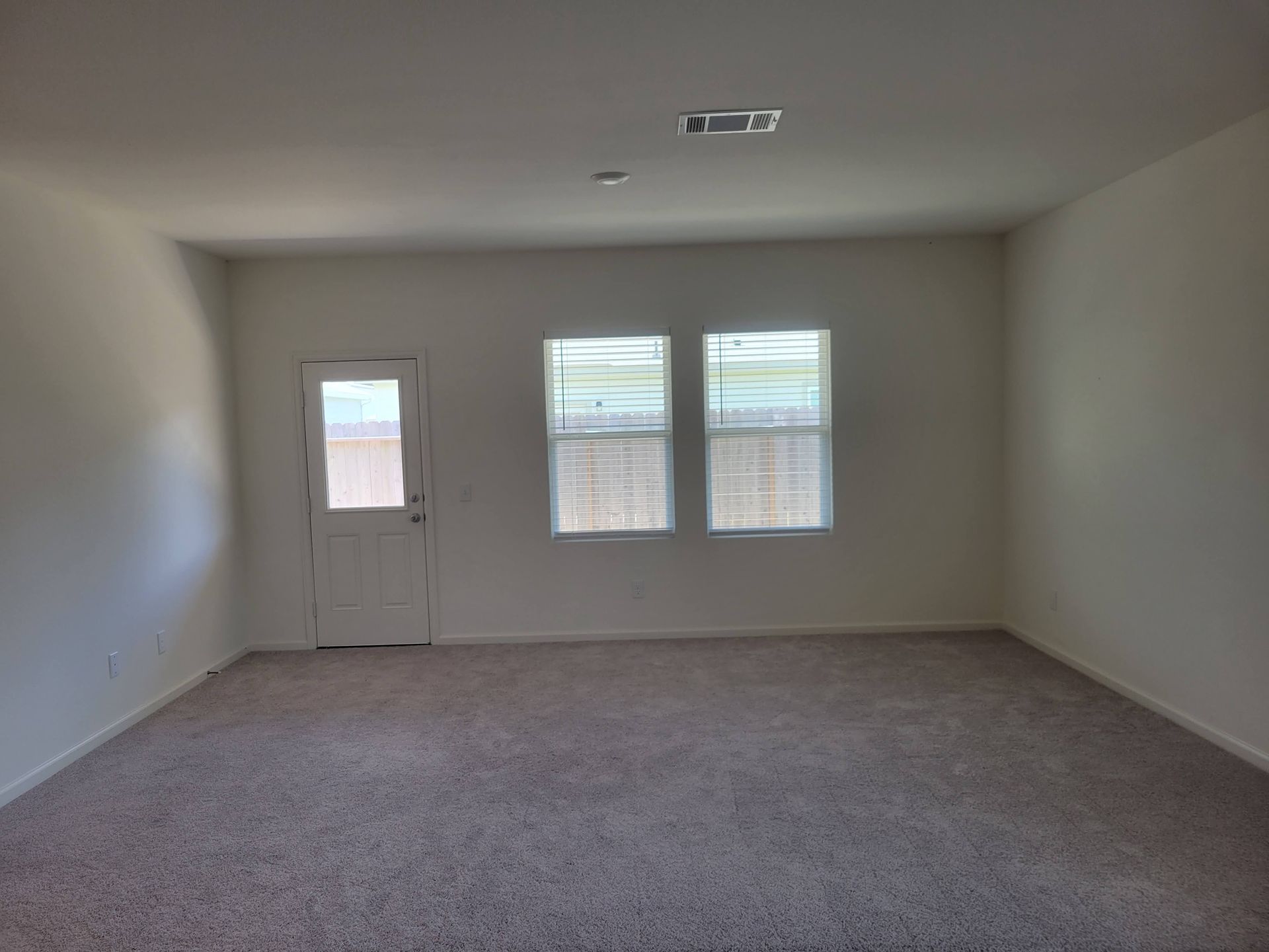 Empty room with beige carpet, white walls, a door, and two windows.
