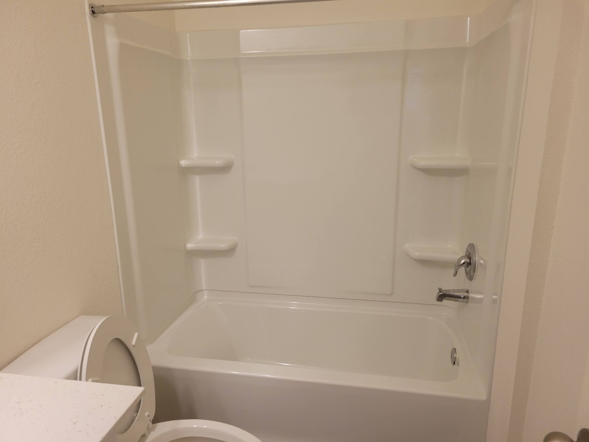 White bathroom with a tub, shower surround, and toilet.