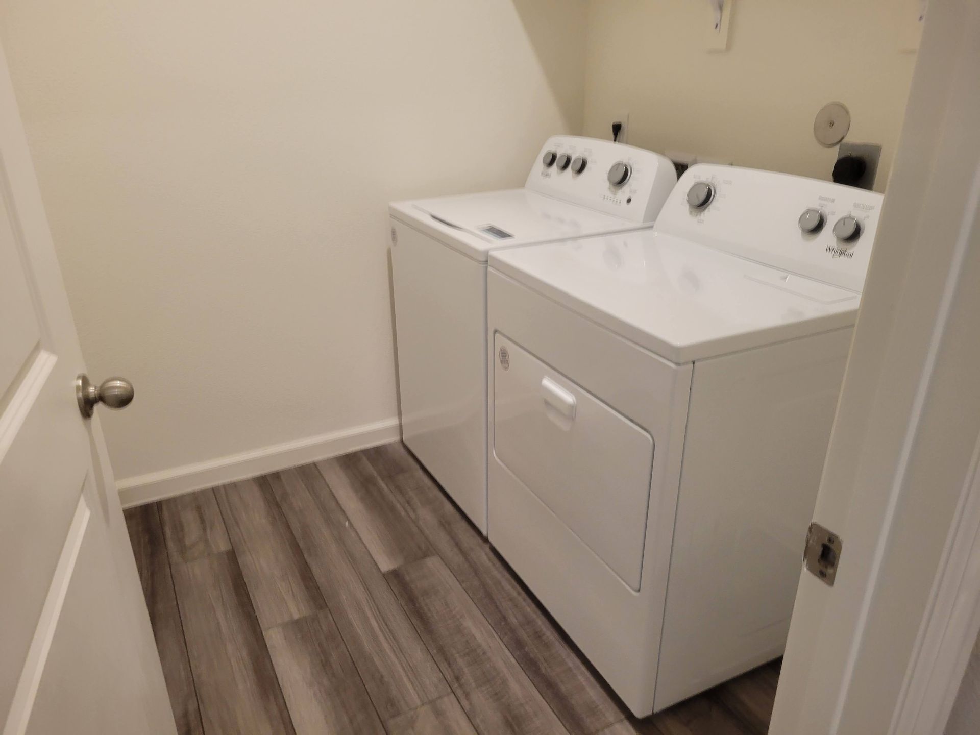 White washer and dryer in a laundry room with gray wood-look flooring and white walls.