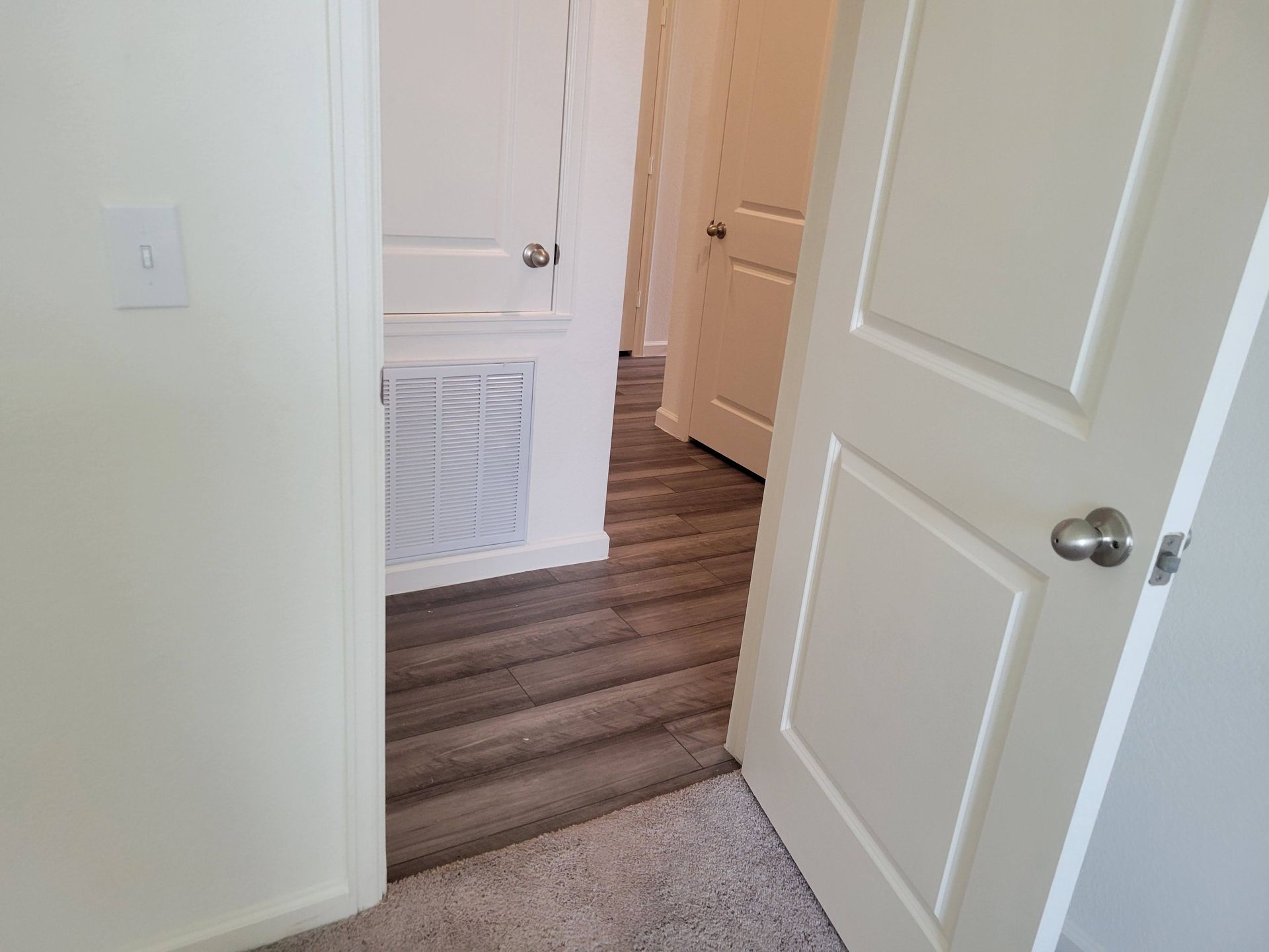 Open doorway leading to hallway with doors, gray flooring, and white walls.