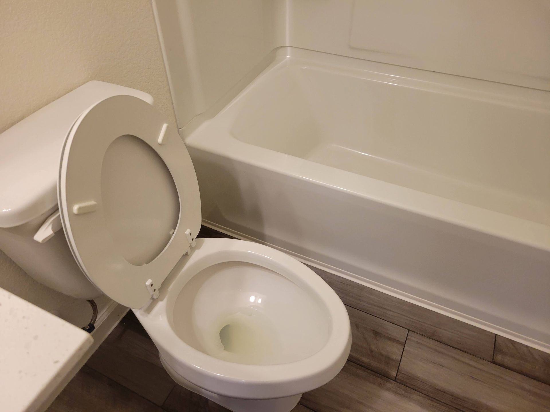 Toilet with open seat next to a bathtub in a bathroom.