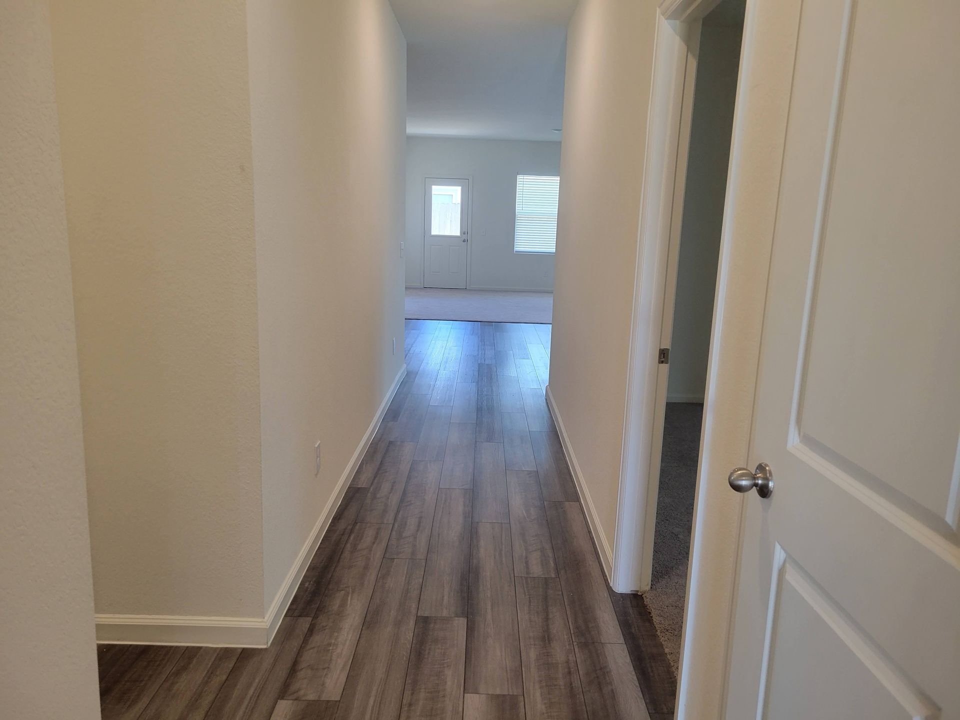 Hallway with gray wood-look flooring, white walls, and a partially open door to a room.
