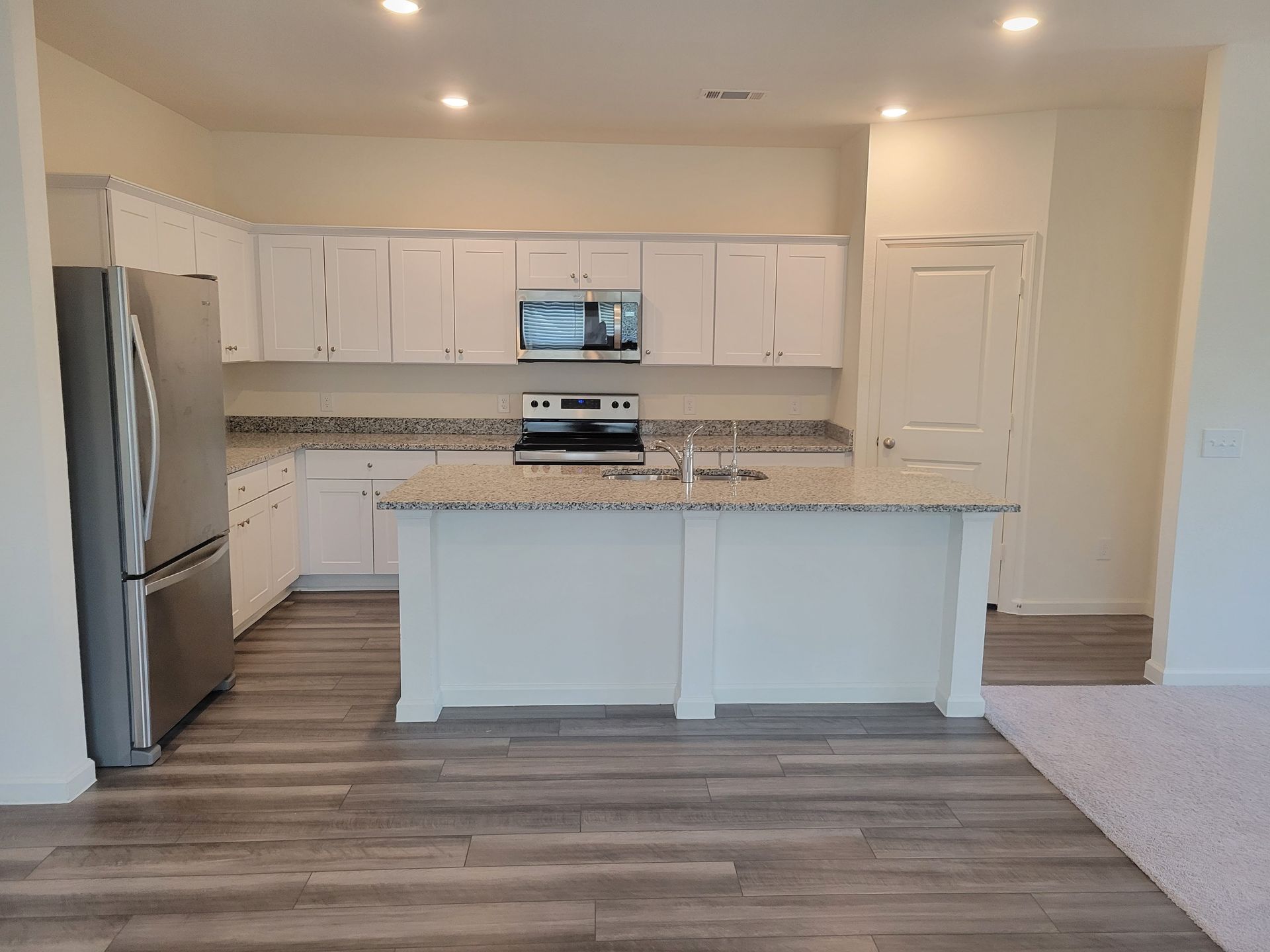 White kitchen with stainless steel appliances, granite countertops, and light wood flooring.