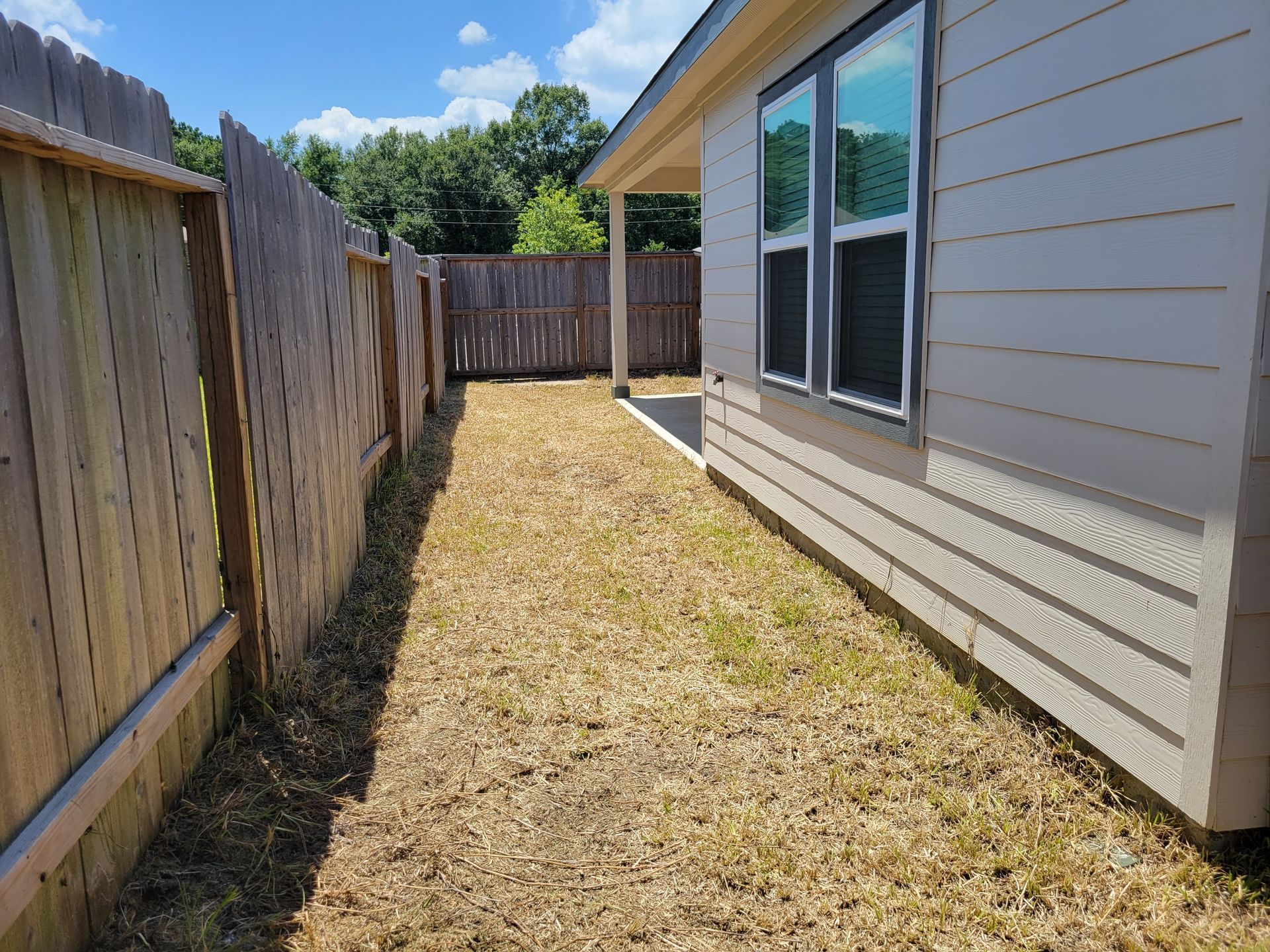 Narrow backyard with wooden fences on either side and the side of a house.