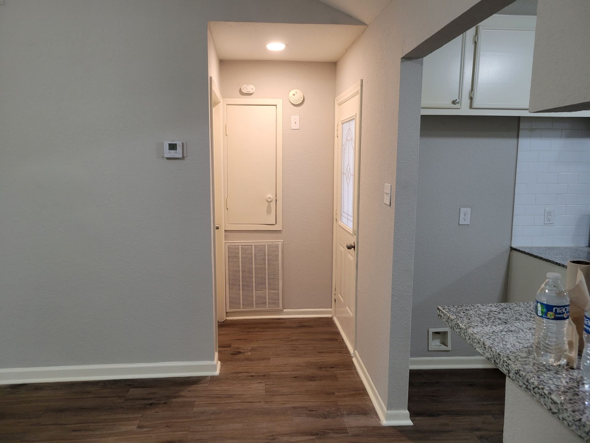 Hallway with grey walls, dark wood floor, and doorway to kitchen.