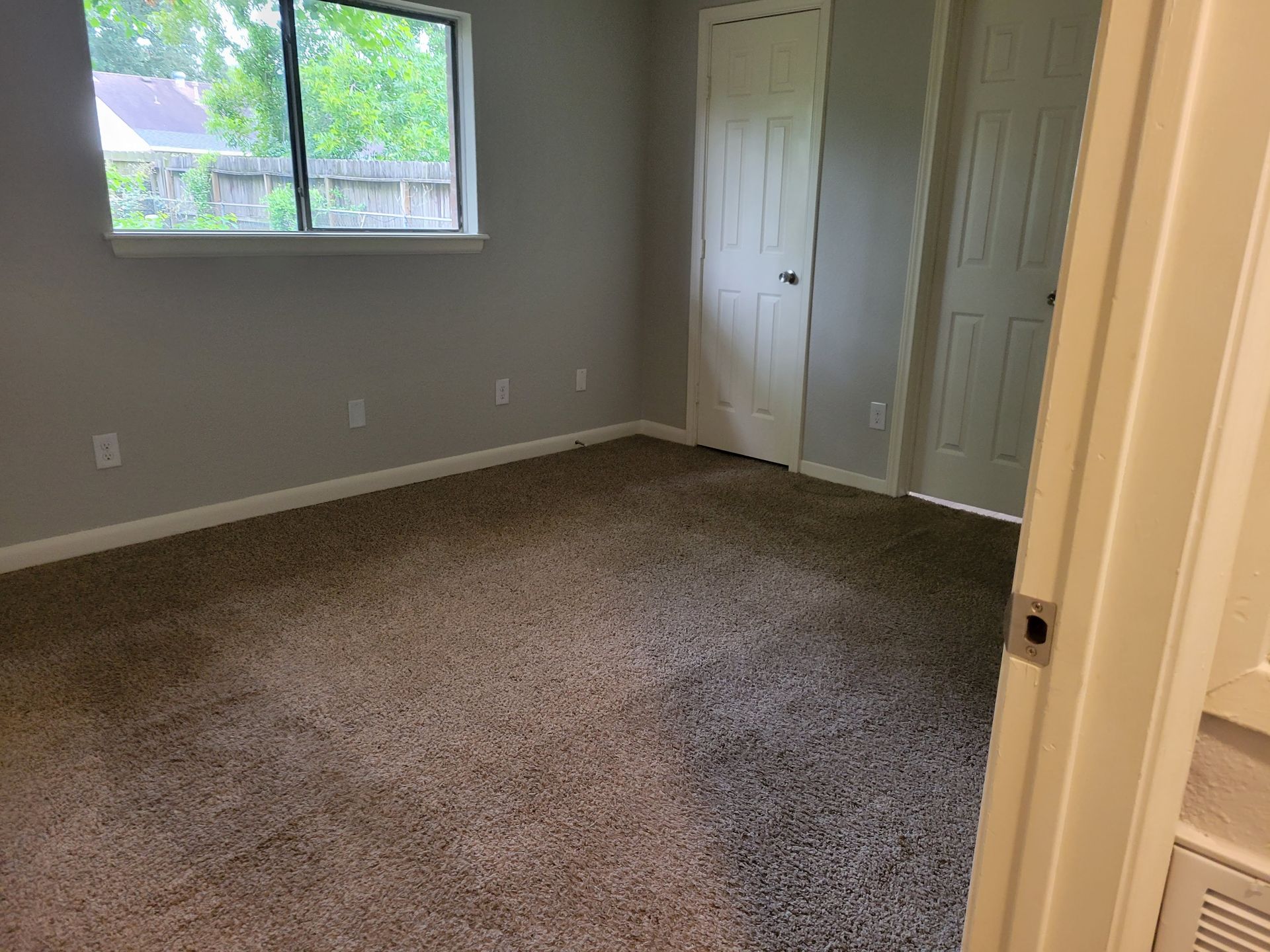 Empty bedroom with gray walls, two white doors, a window, and brown carpet.