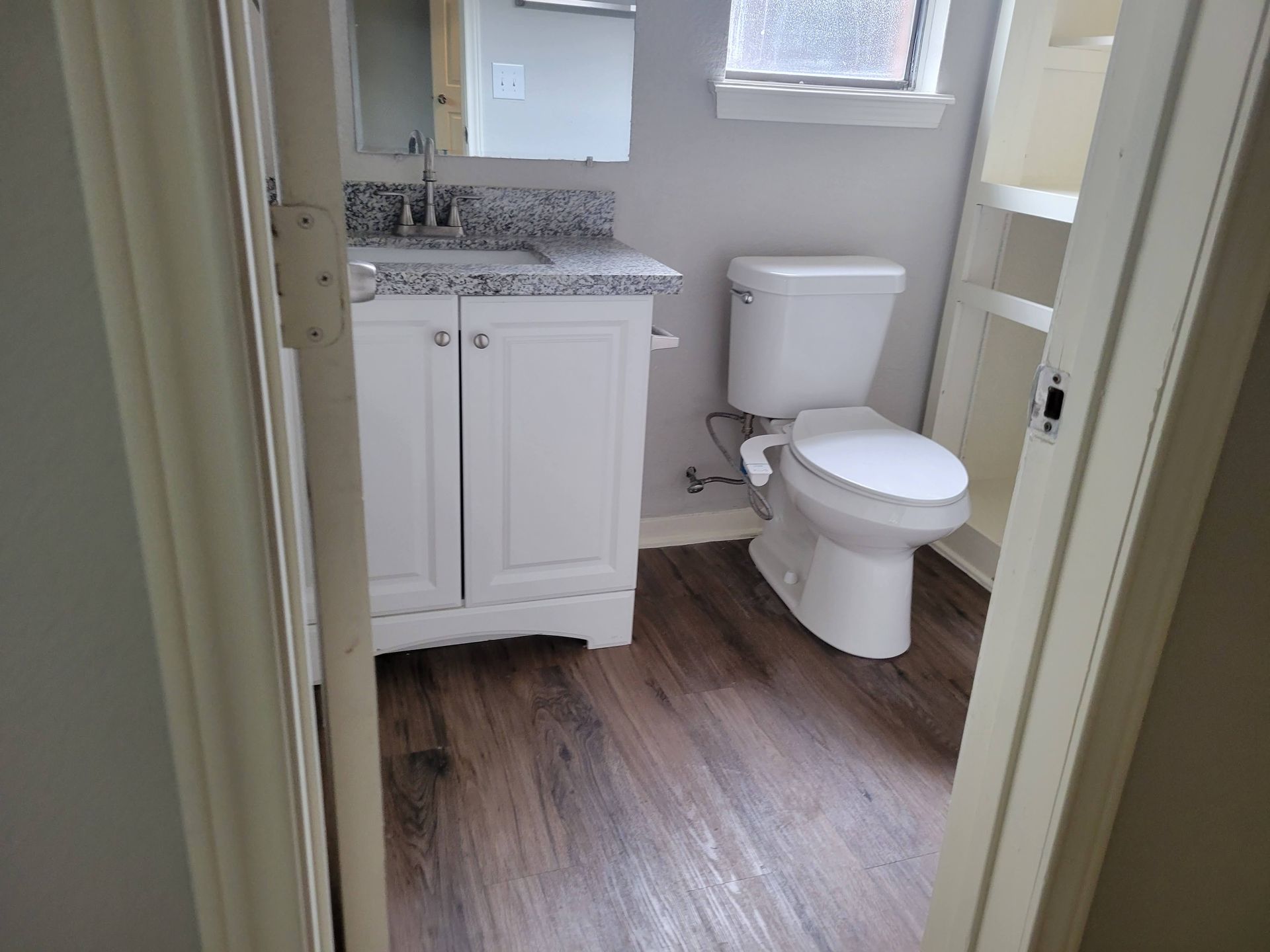 Bathroom with white vanity and toilet, gray countertop, and dark wood-look flooring.