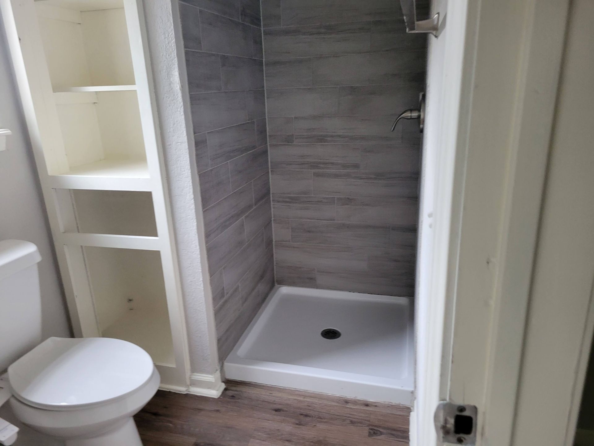 Bathroom with a tiled shower, built-in shelves, and a toilet. The shower has a white base and gray tiles.