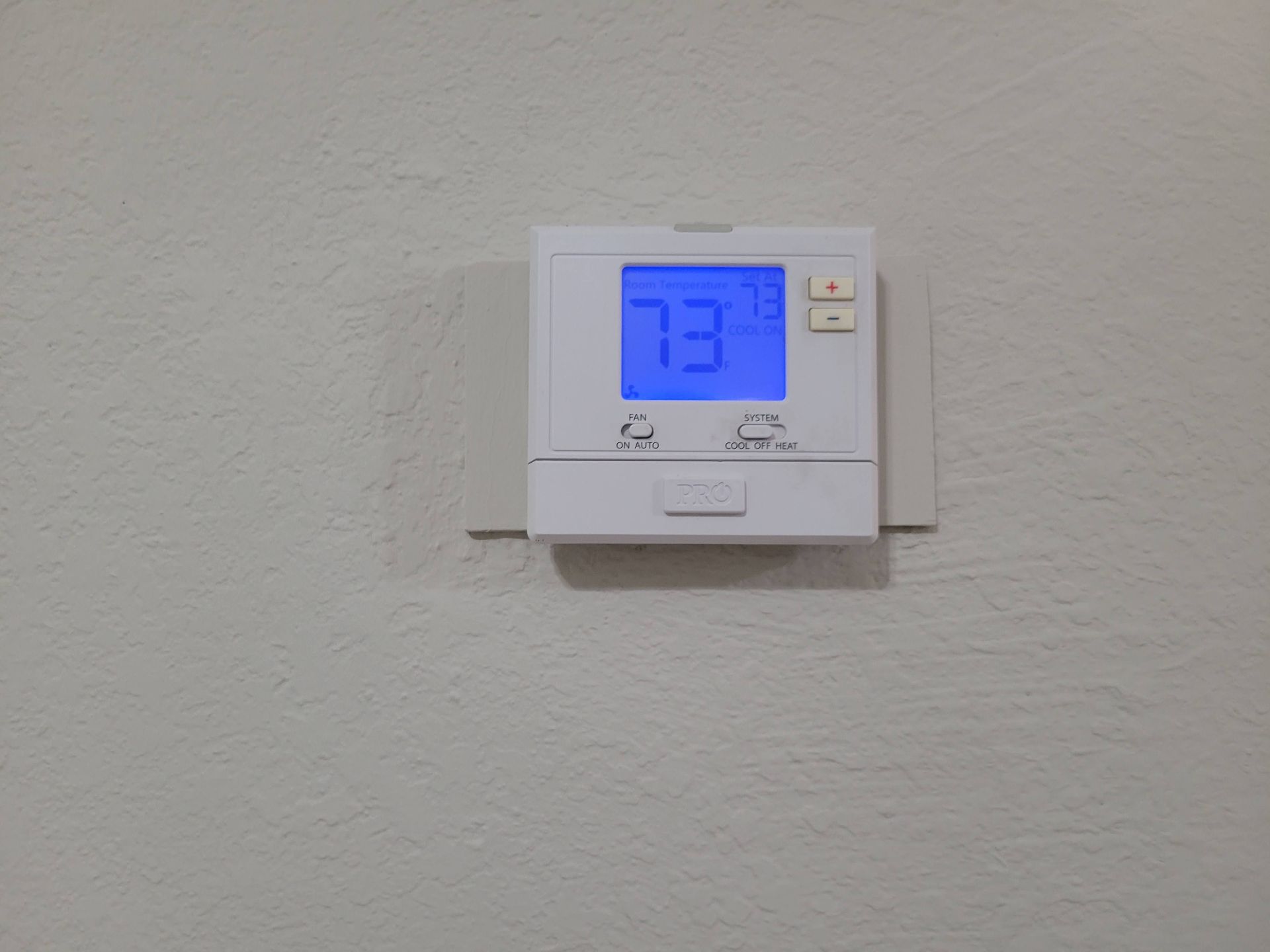 White thermostat displaying 73°F on a white wall.