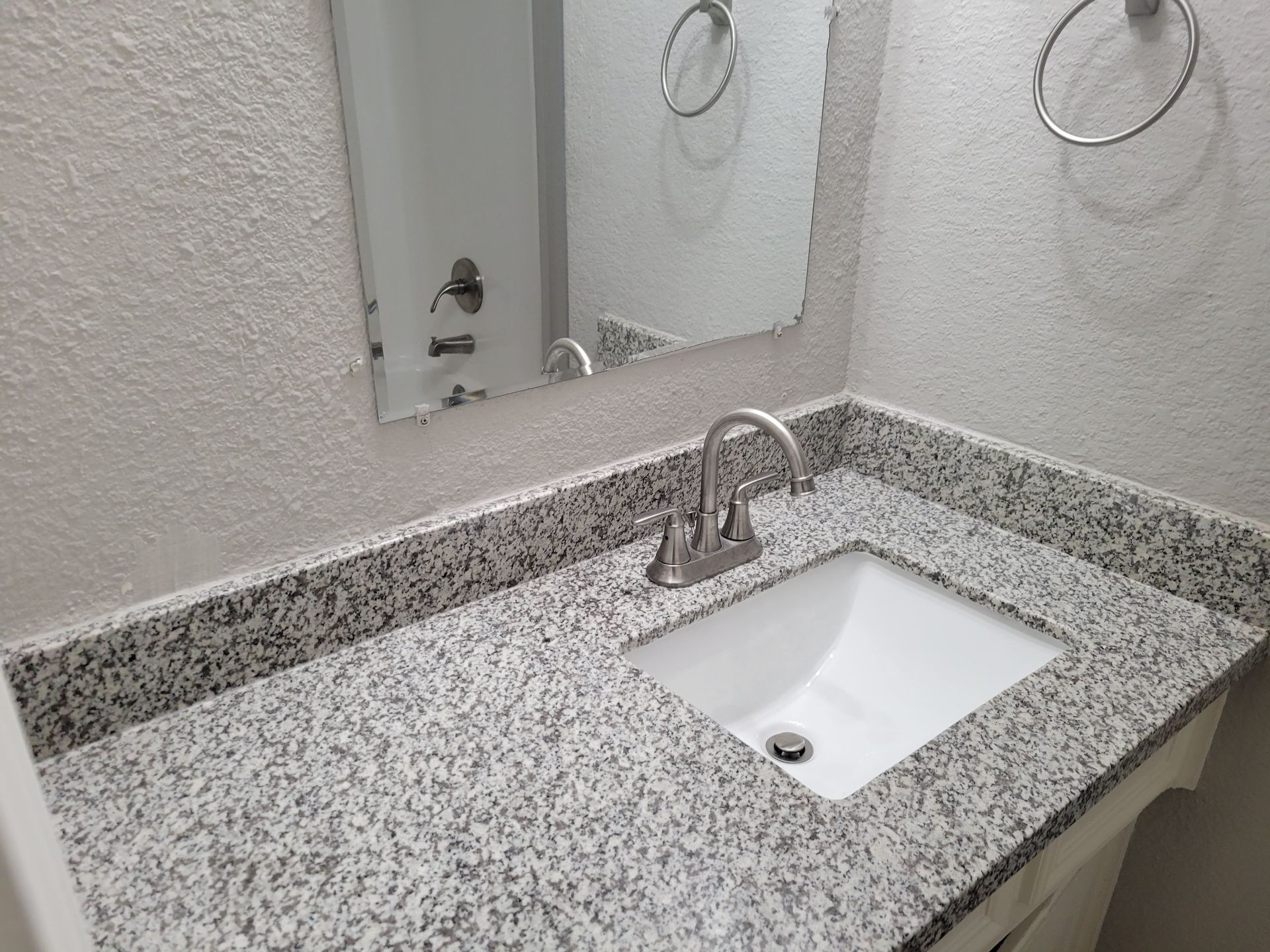 Bathroom vanity with a white sink, granite countertop, and mirror.