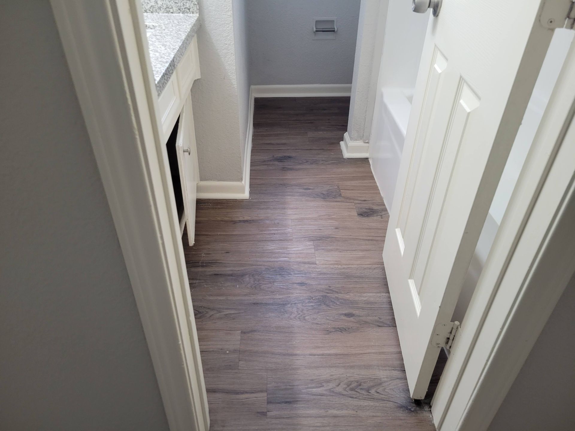 Bathroom with wood-look flooring, white trim, and a partially open door. Gray walls and a countertop are visible.