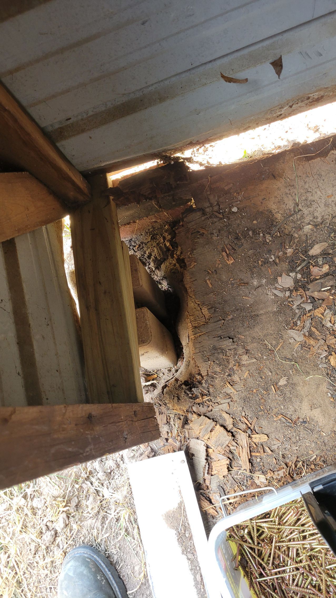 Hole in ground next to wooden deck with dirt, debris and sunlight.