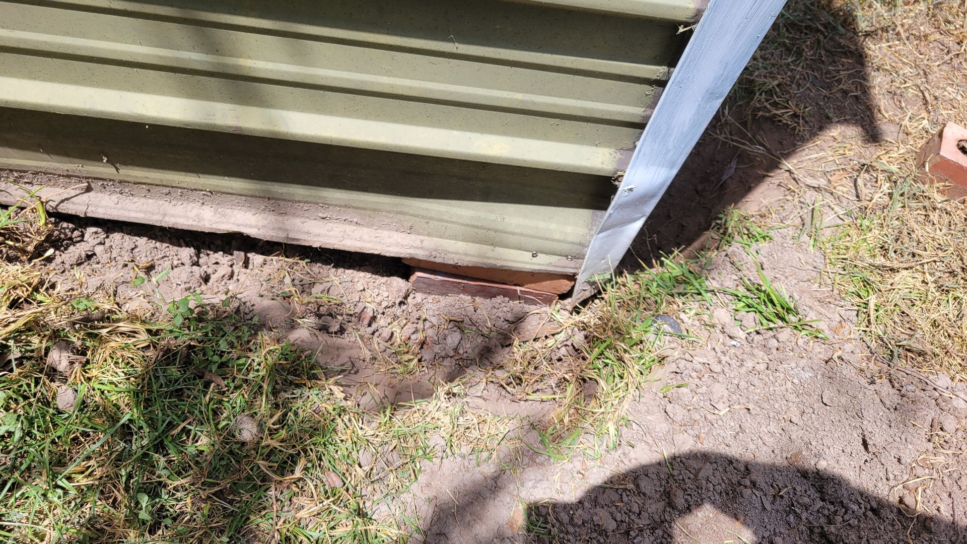 A metal shed with a gap at the base, exposing the ground.