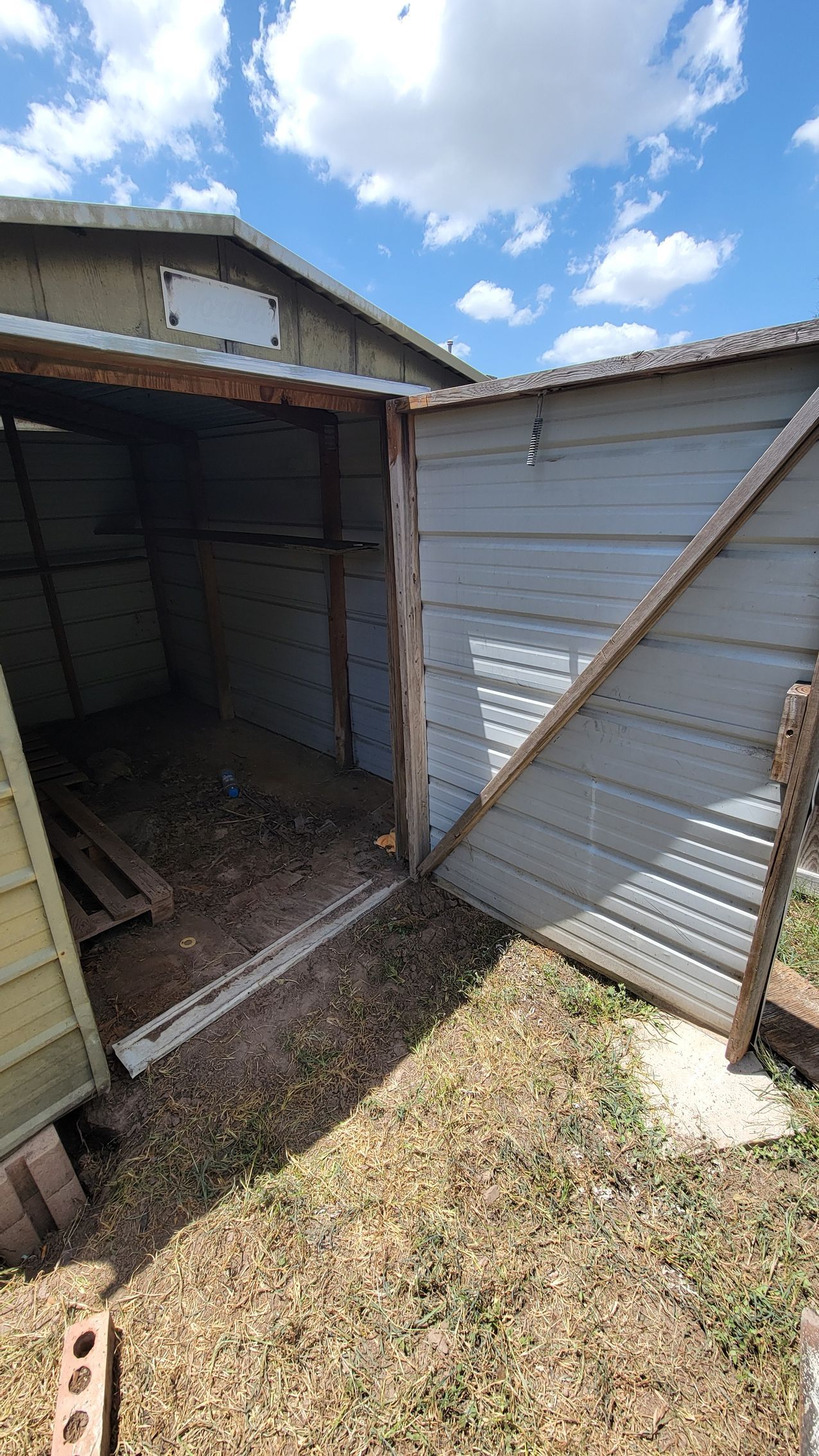 Dilapidated shed with open door, weathered blue siding, and dirt floor under a cloudy sky.