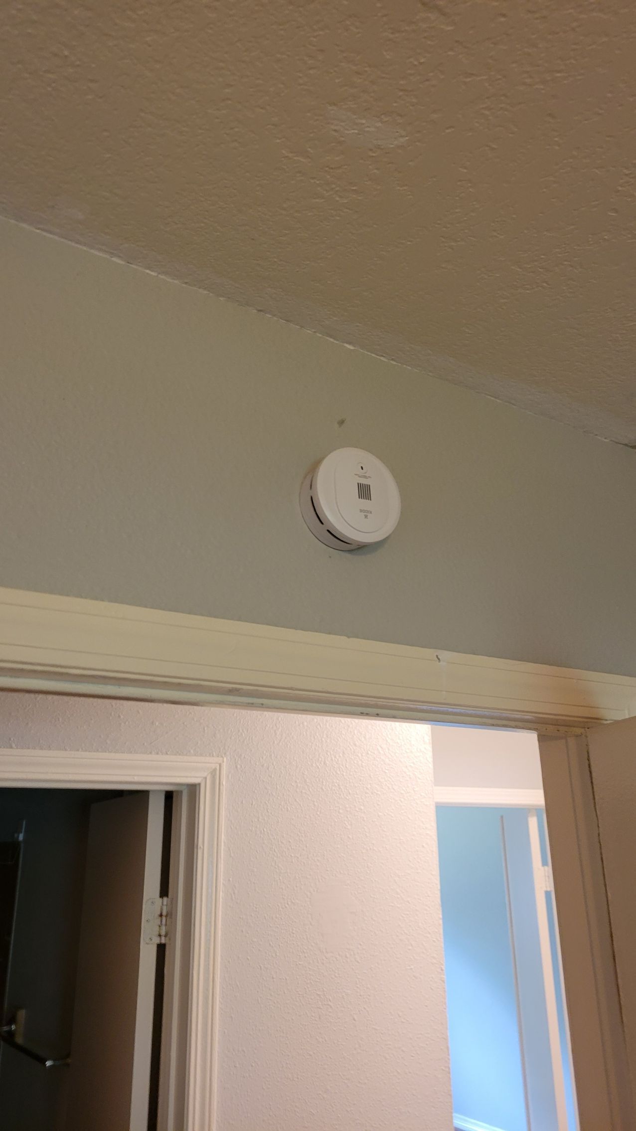 White smoke detector on a gray wall, near a doorway.