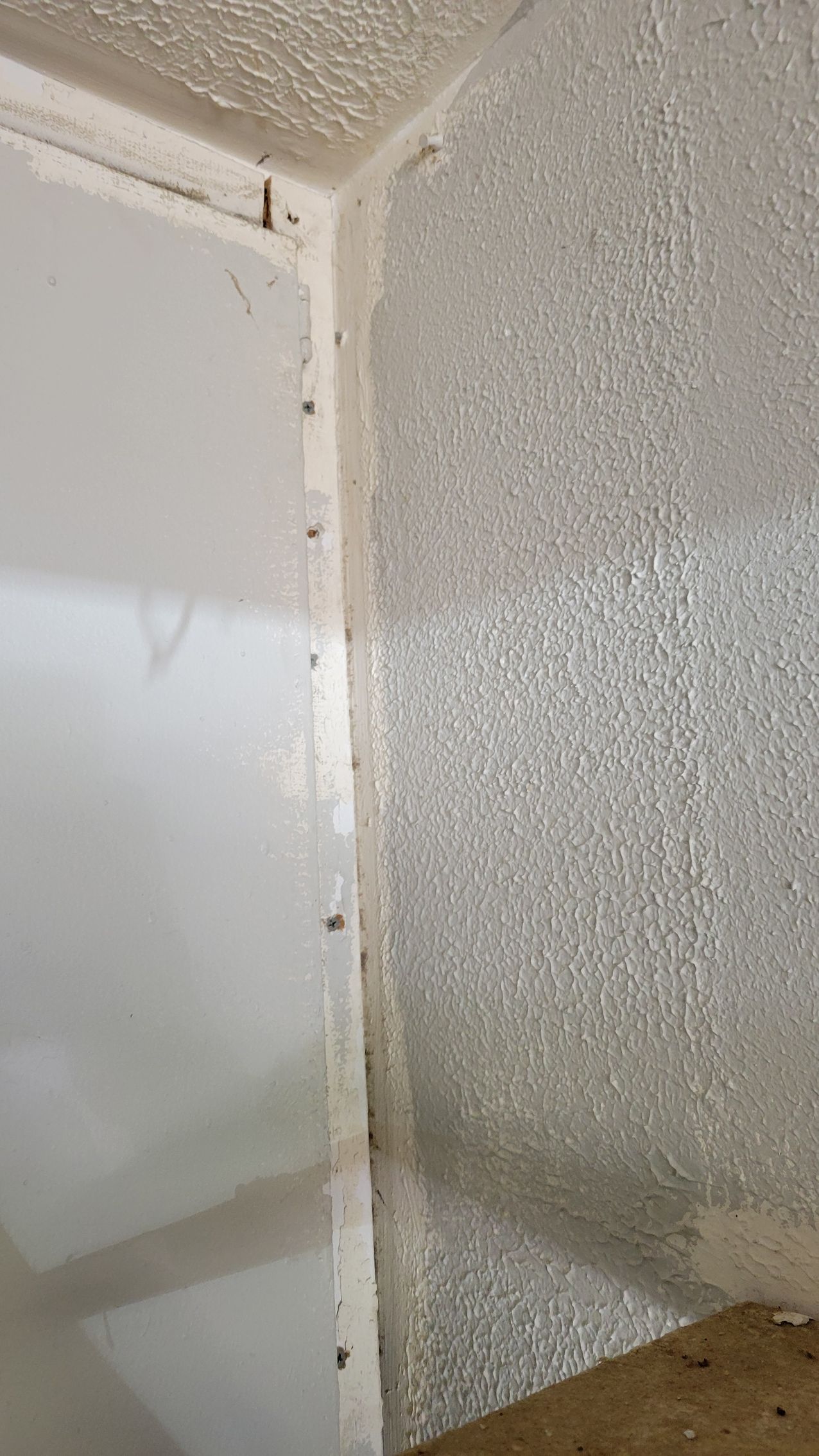 Corner of a room; white wall meets textured, silver-colored wall. Fasteners visible along the seam.