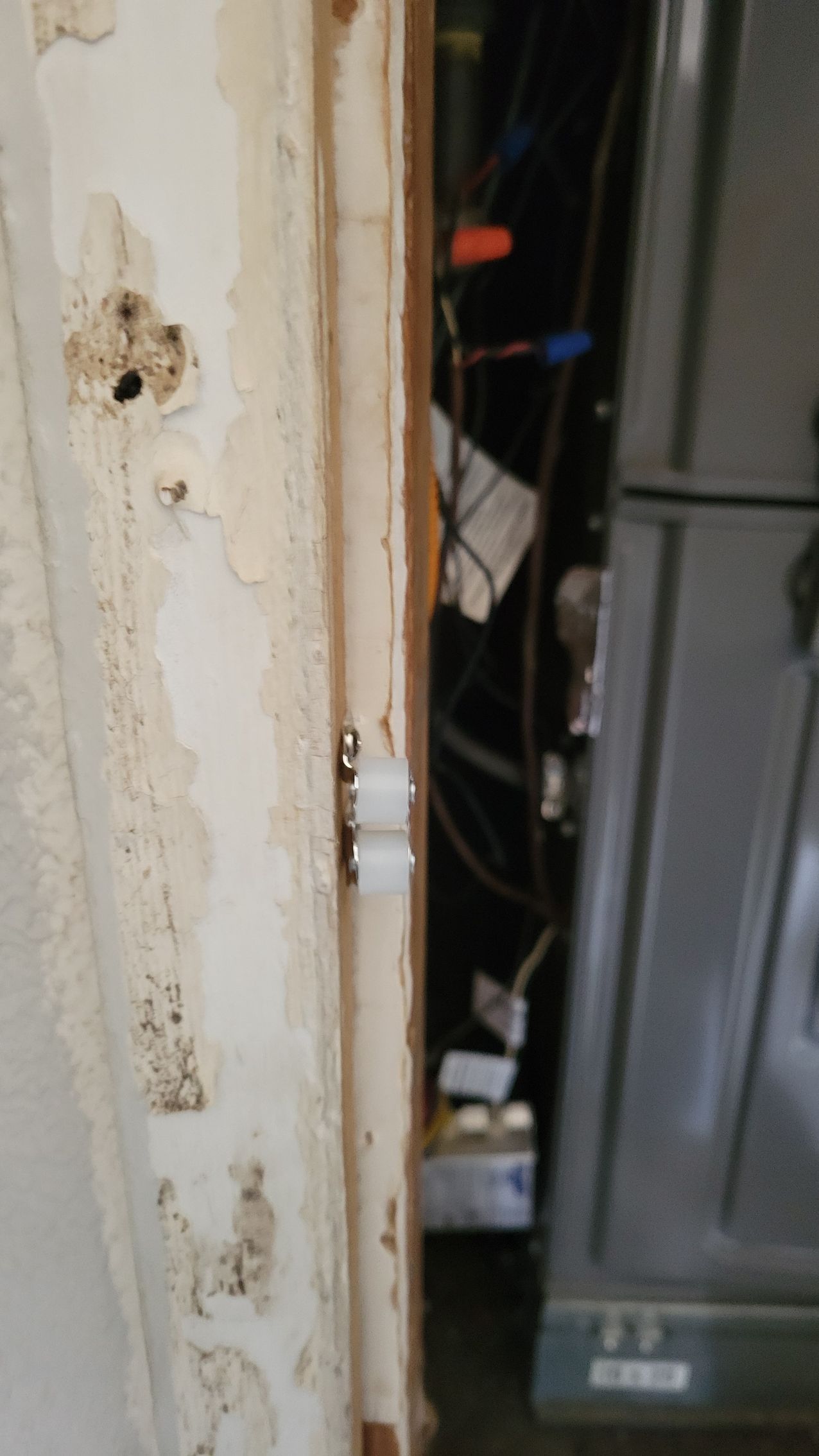 White roller hardware on a door frame, with visible discoloration and an air conditioning unit in the background.
