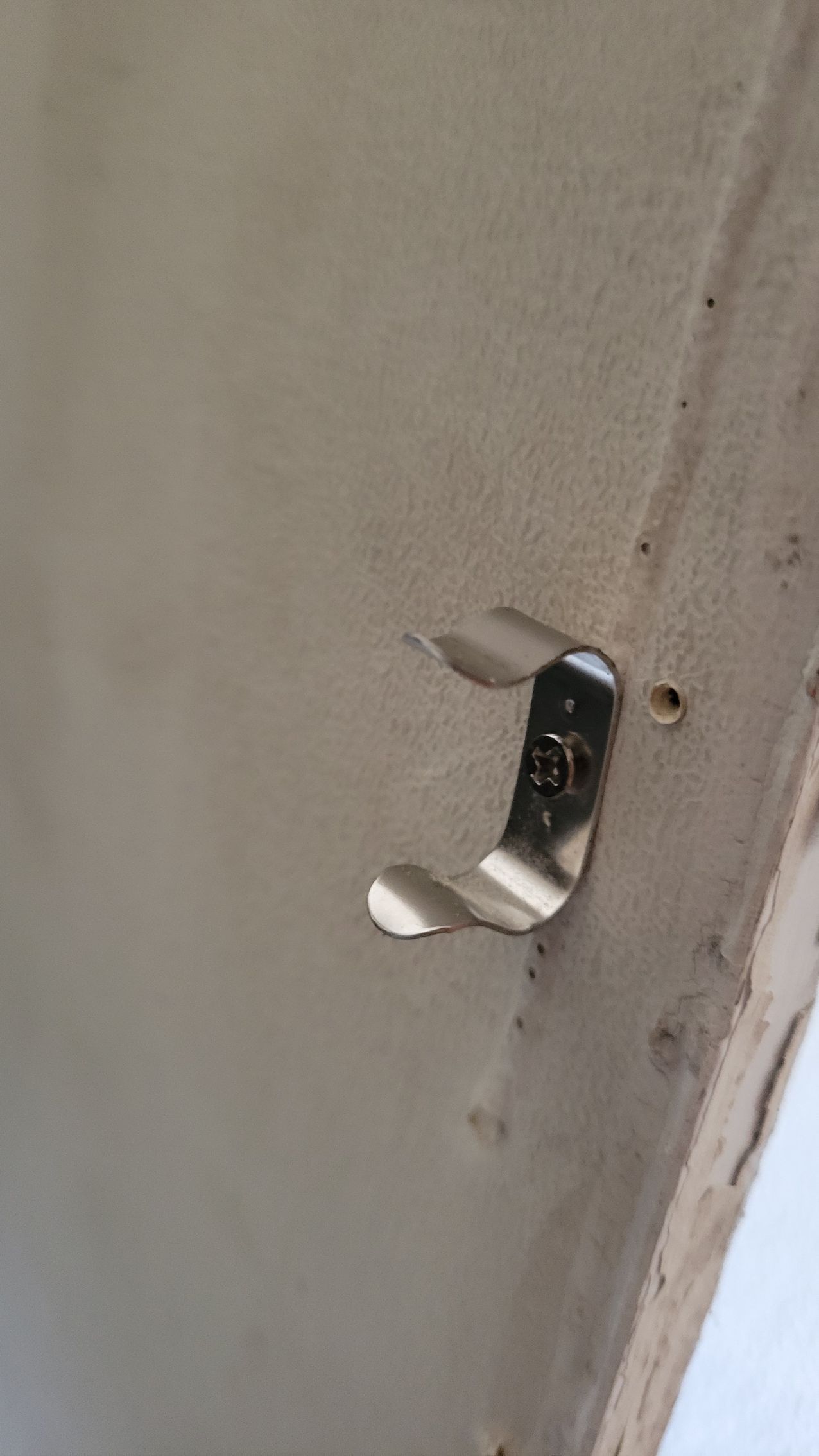 A metal clip screwed to a light-colored surface; a small hole is visible.
