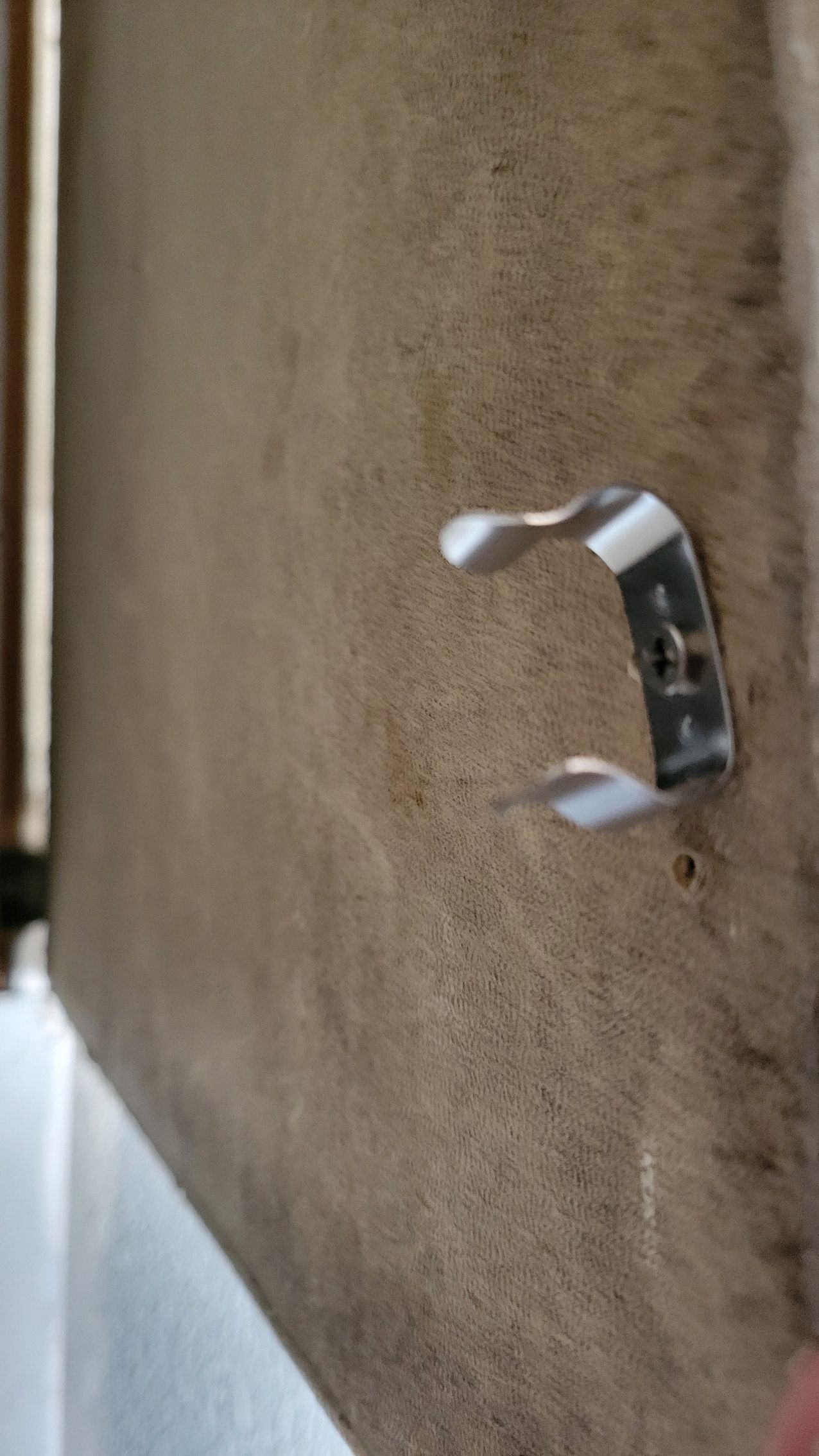 Metal clip attached to a textured, light brown surface.