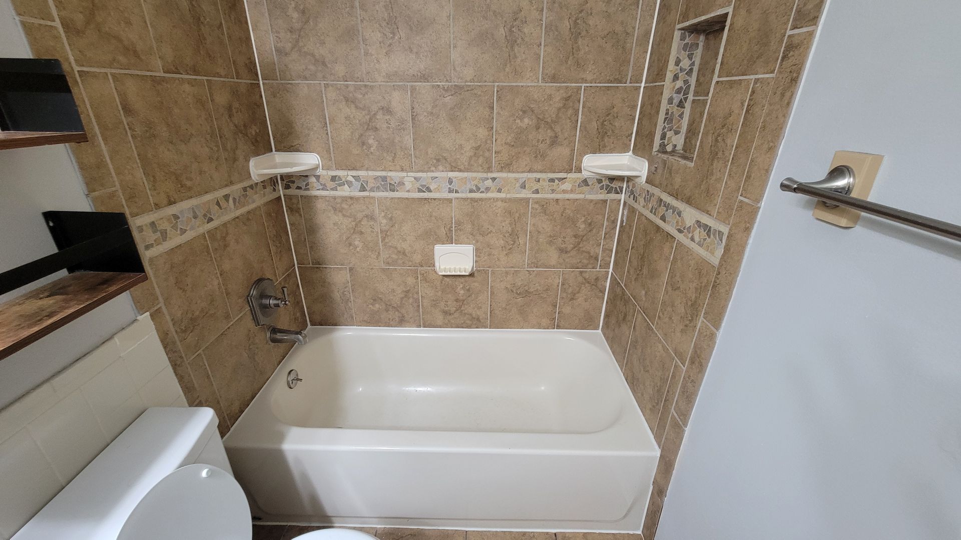 Bathroom with a white bathtub and brown tiled walls.