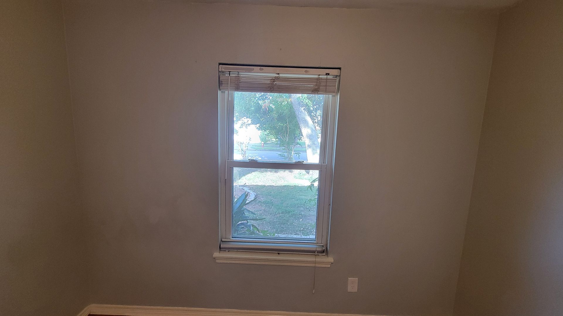 Interior view of a room with a window centered on the grey wall; view of outside is partially obscured.