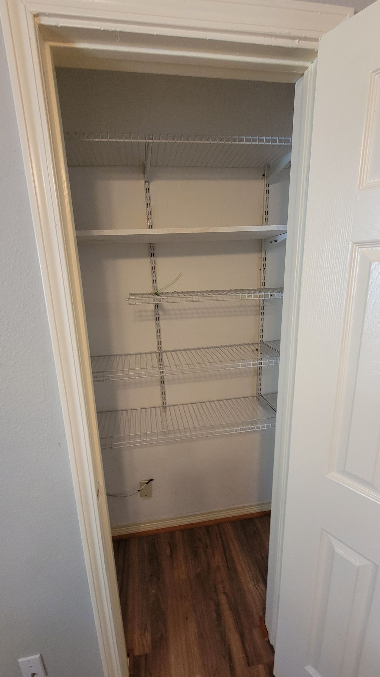 Empty closet with wire and solid shelves, wood floor, white door and trim.