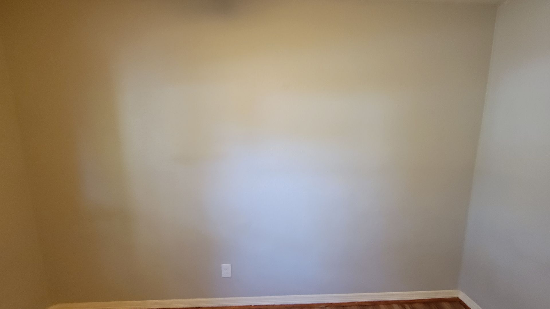 Beige walls in a room with a wood floor and an electrical outlet.