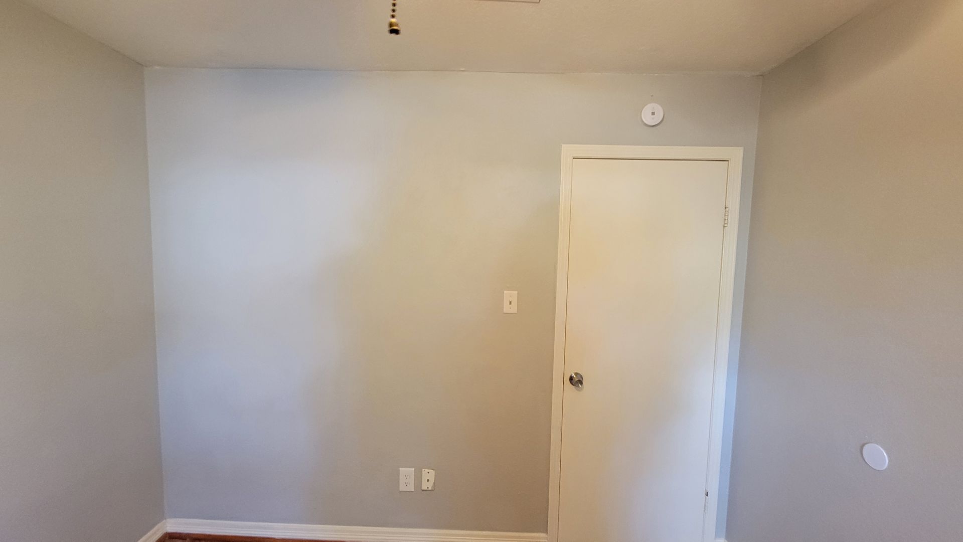 Gray painted interior room with a white door, outlet, and smoke detector.